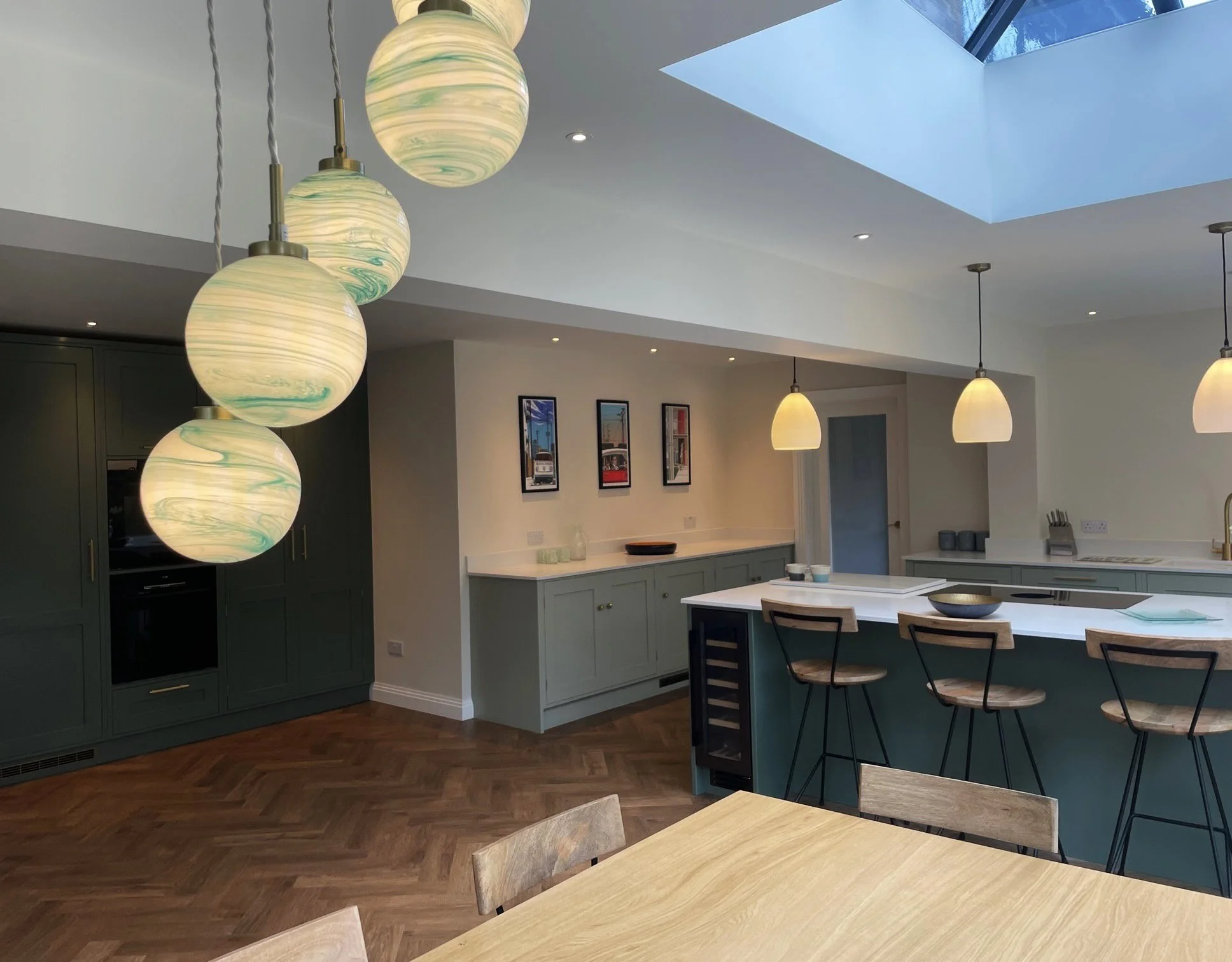 Modern kitchen with green cabinetry, a white countertop island with bar stools, pendant lights, a skylight, and hardwood flooring.