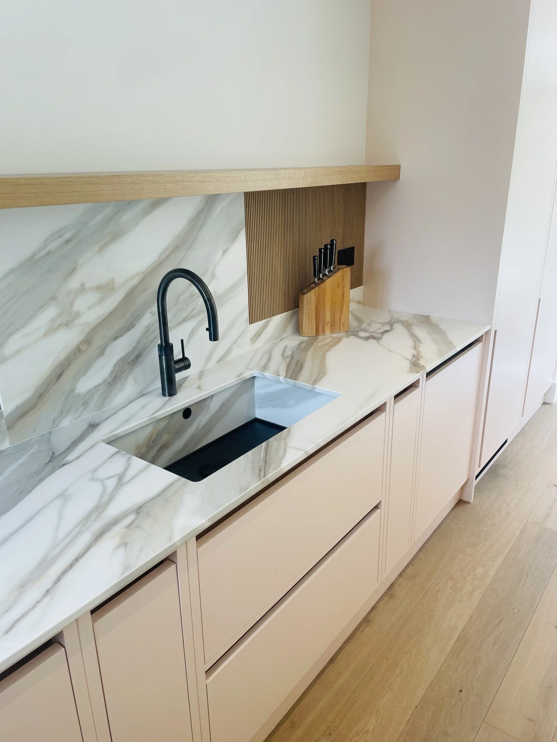 Modern kitchen with a marble countertop, black sink, black faucet, knife block, and beige cabinetry.
