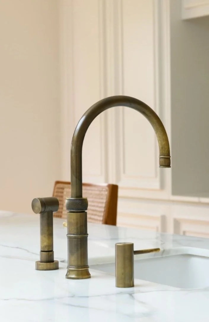 Brushed gold kitchen faucet on a white marble countertop with a soap dispenser and a soap pump.