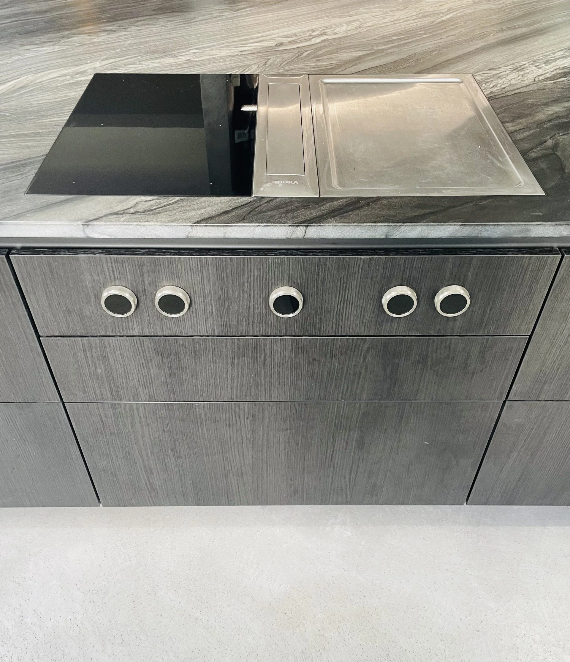 Modern kitchen workspace with built-in induction cooktop, stainless steel sink, and dark wood cabinets.