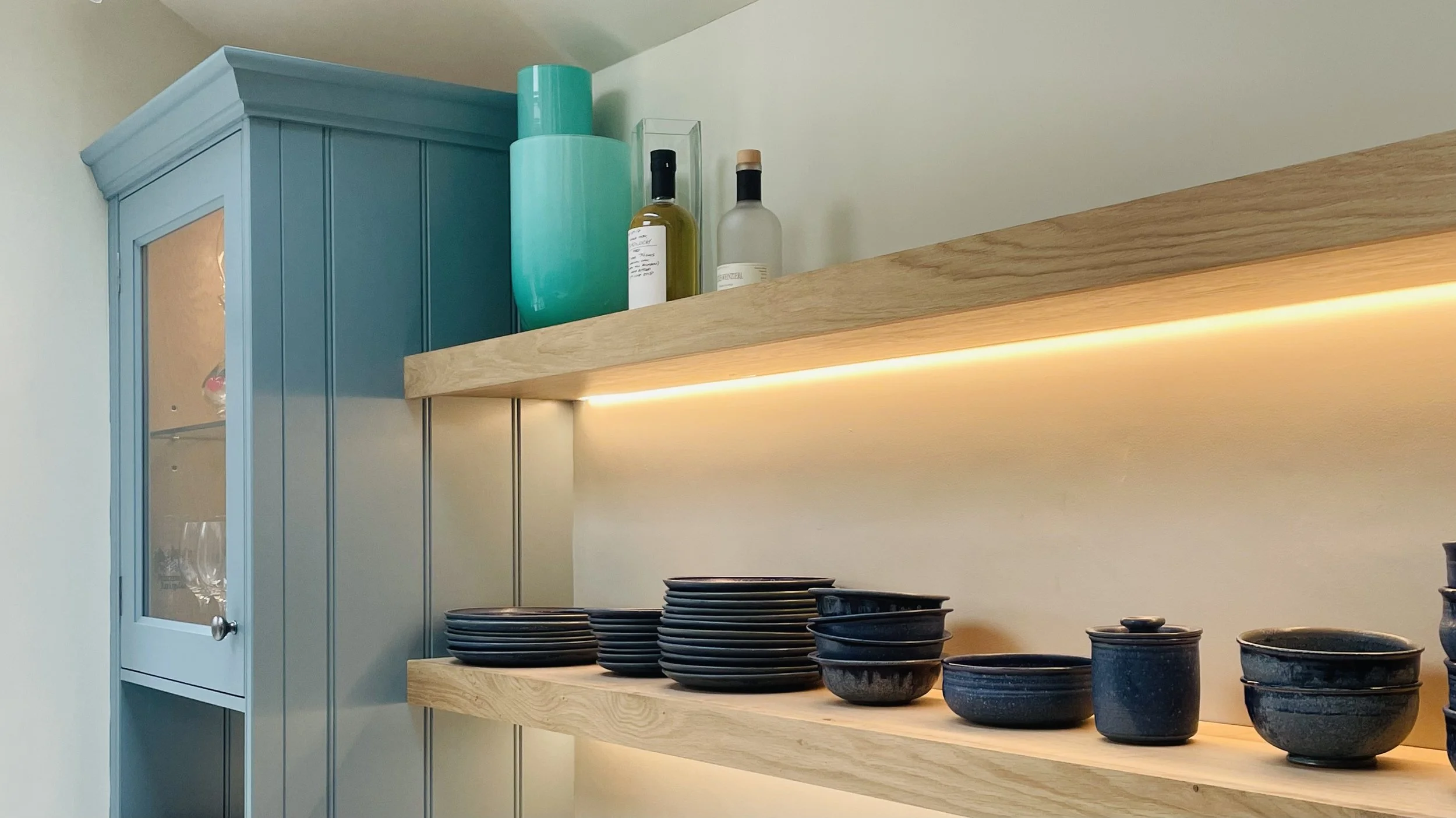 Kitchen shelf with black bowls and a cabinet with glass door, with decorative vases on top.