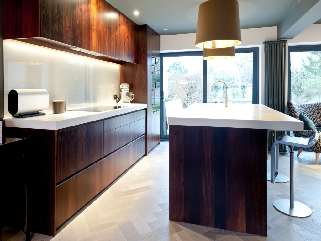 Modern kitchen with dark wood cabinets, white countertop, and large windows with a view outside, featuring a kitchen island with a white surface and modern barstool.