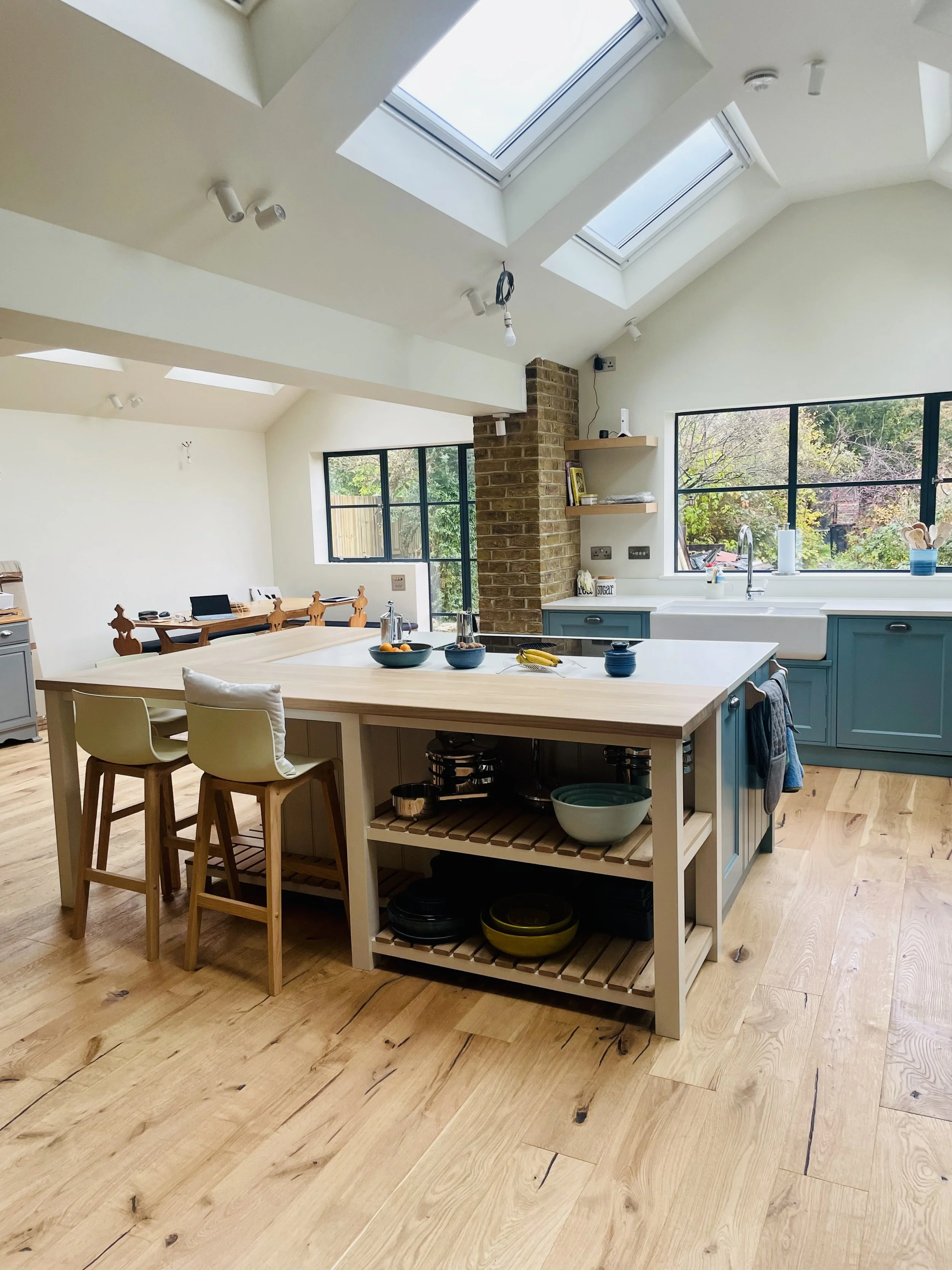 Bright kitchen with skylights, blue cabinetry, an island with open shelving, and a dining area in the background.