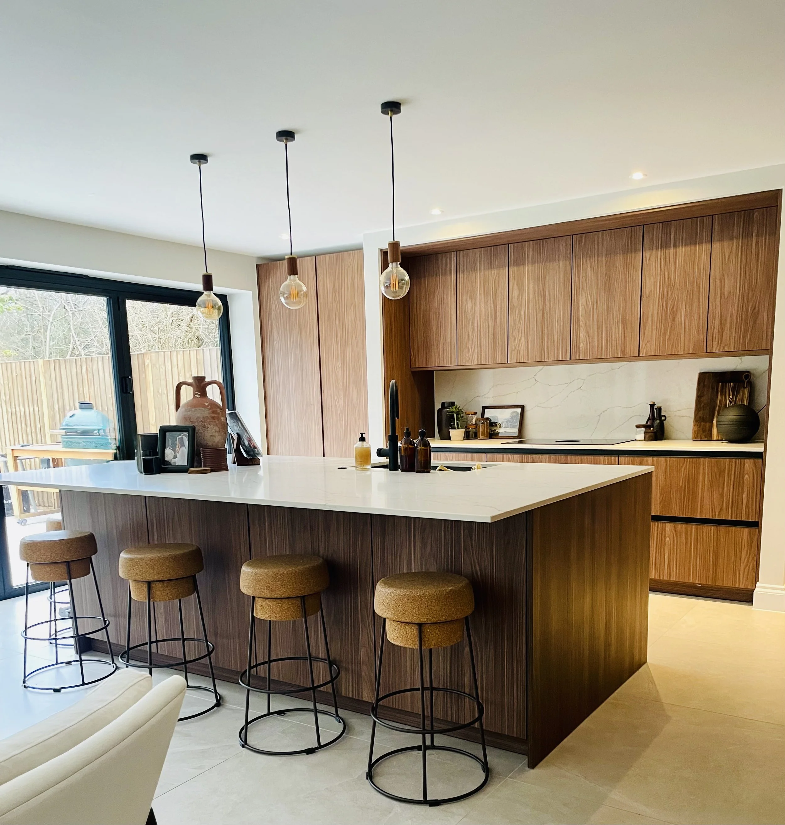 Modern kitchen with a large white island, four mustard-colored bar stools, wooden cabinetry, and pendant lights.