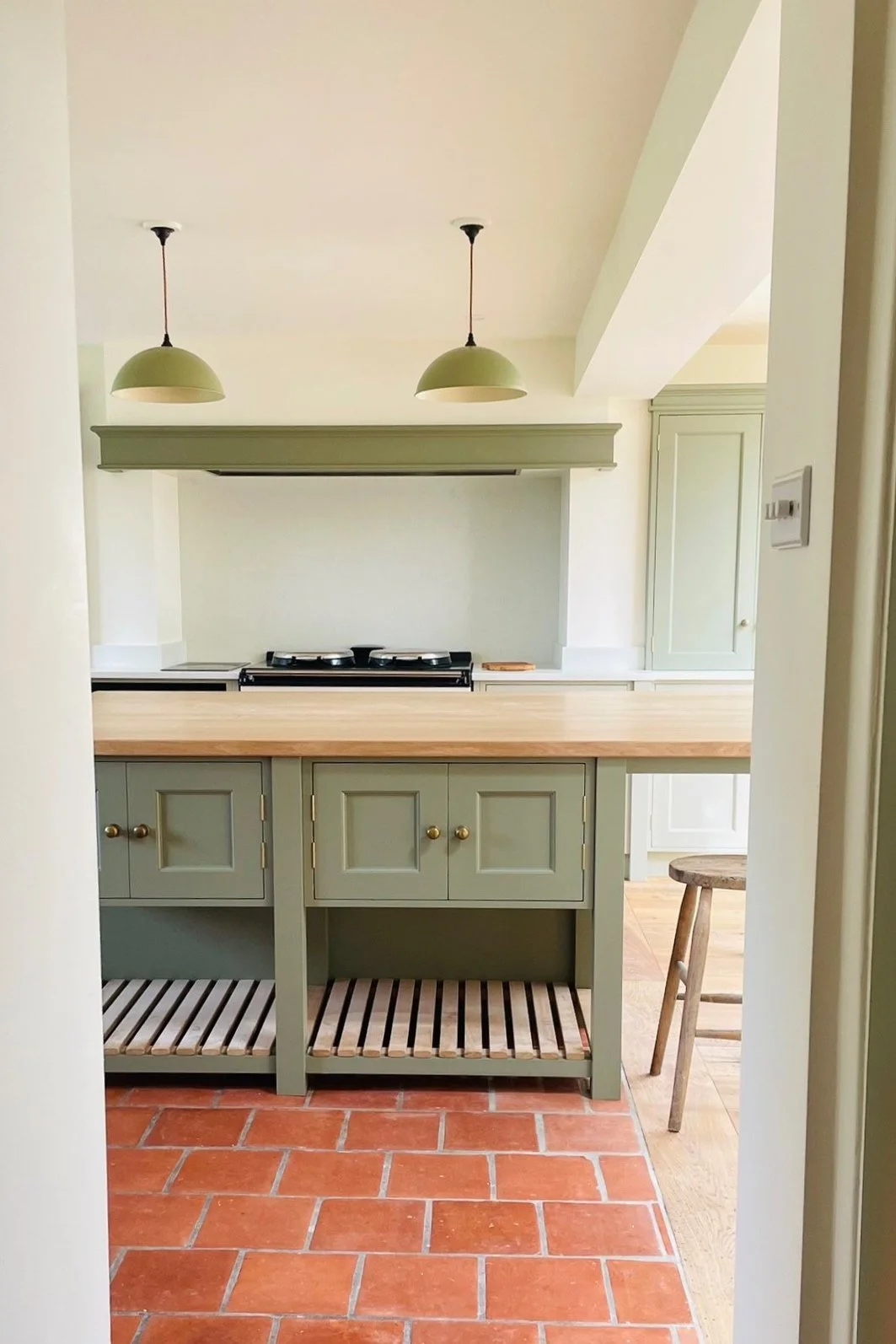 Kitchen with green cabinets and a wooden countertop, two pendant lights, and terracotta tile flooring.