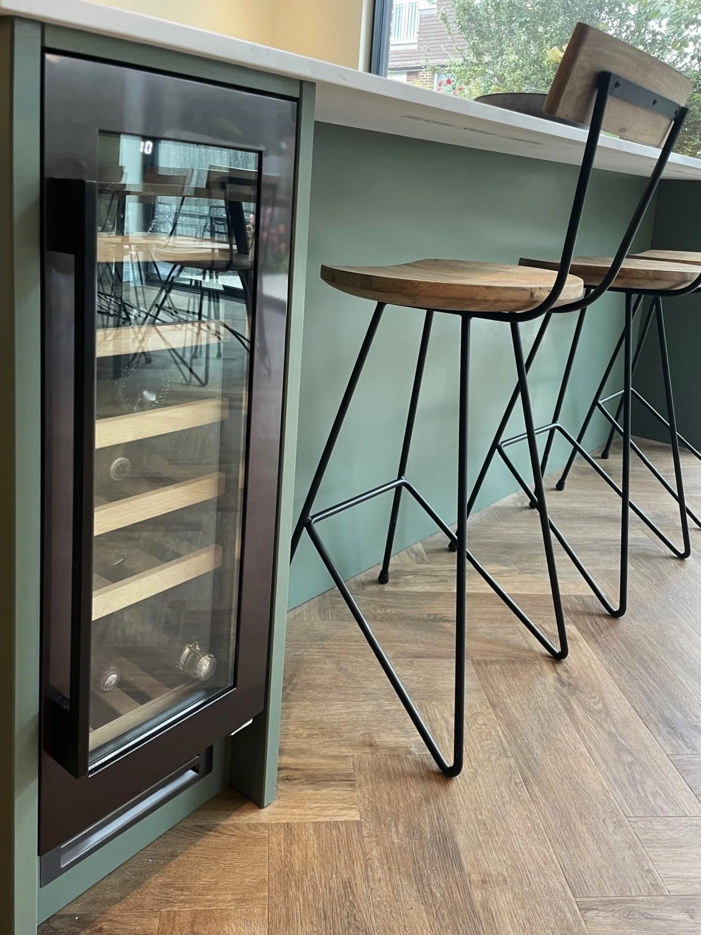 A small wine cooler next to a green counter with wooden bar stools in a modern cafe or restaurant.