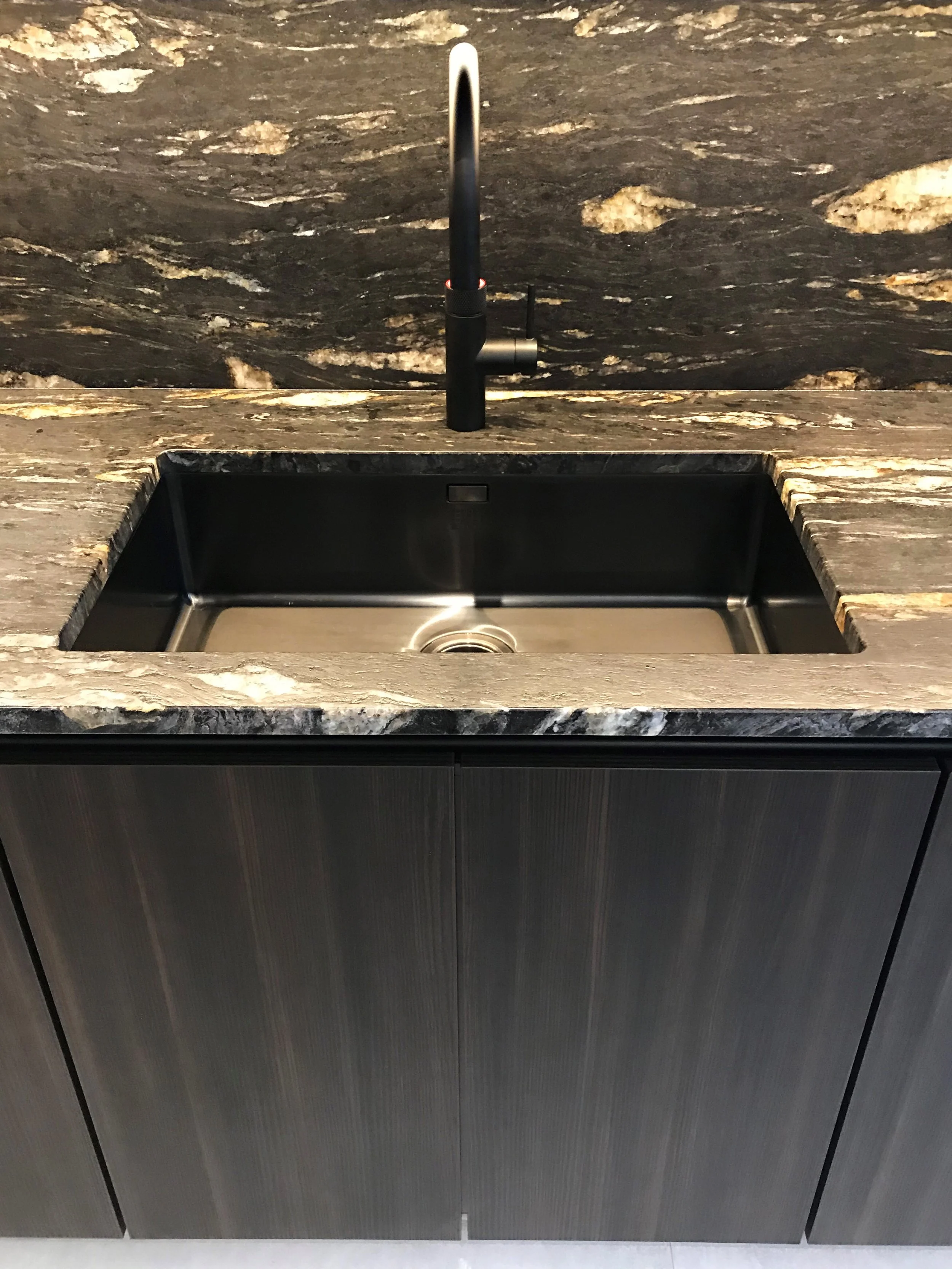 A black kitchen sink with a black faucet, set into a marbled gray countertop and cabinet.