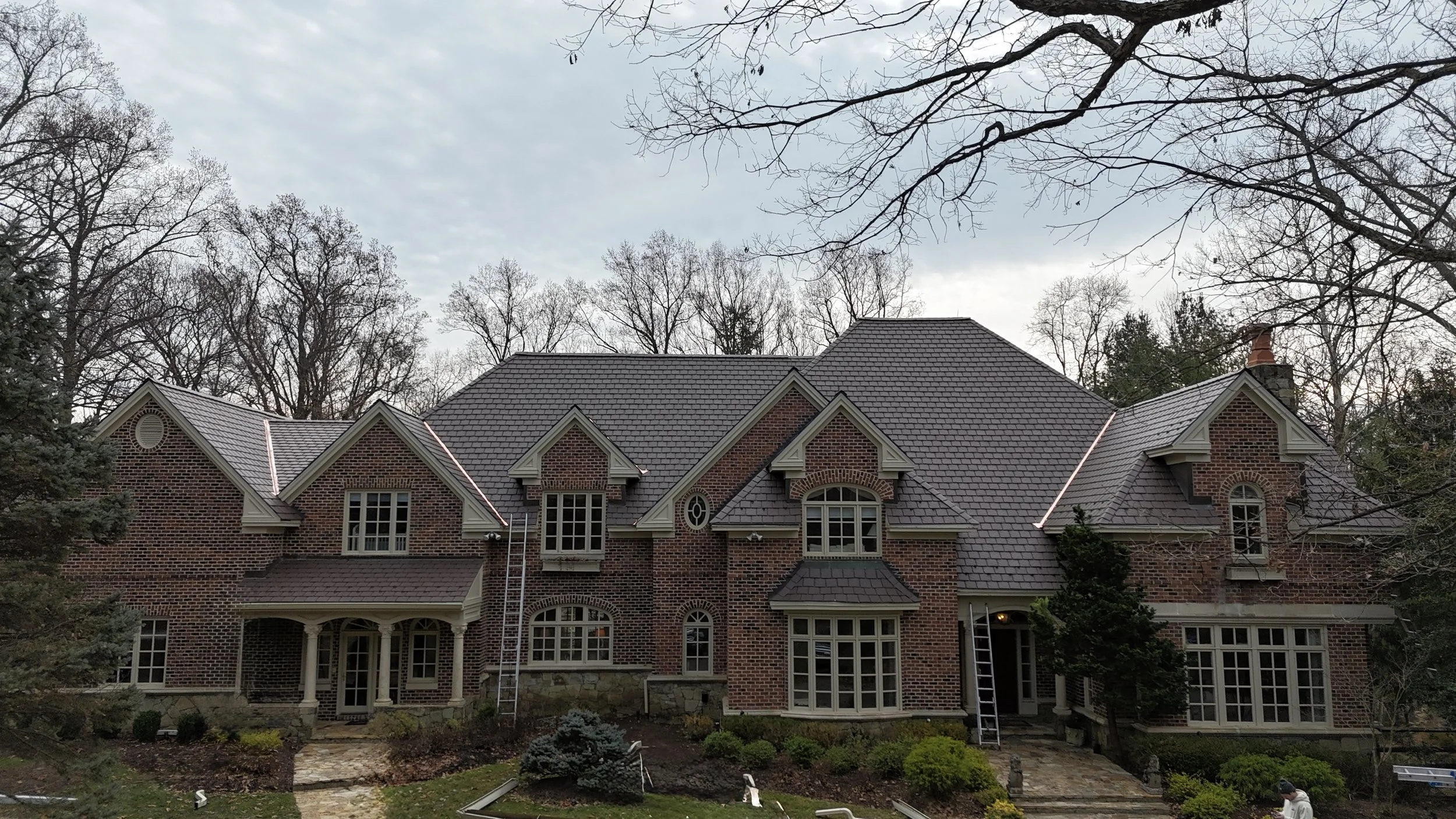 Large brick house with multi-gabled roof, surrounded by trees and landscaped yard.