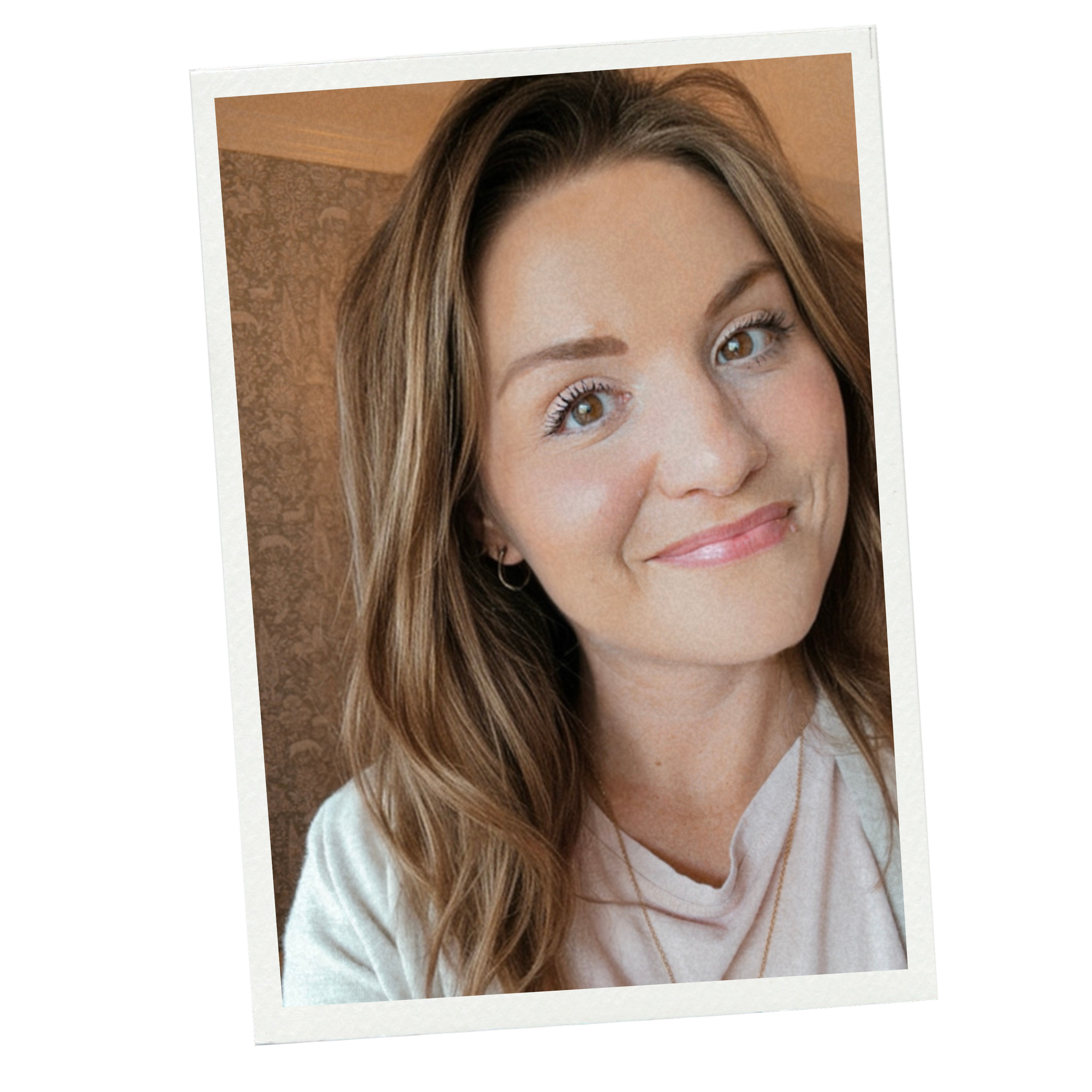 A woman with light brown hair and brown eyes smiling slightly, wearing a cream-colored top, in front of a patterned wall.