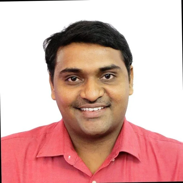 Portrait of a man with short black hair, brown eyes, wearing a pink collared shirt, smiling against a white background.