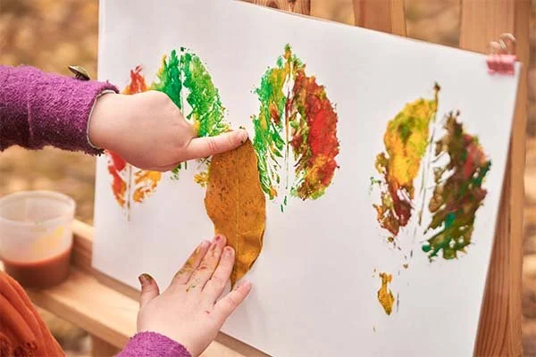 Young child paints with leaves in an outdoor craft project