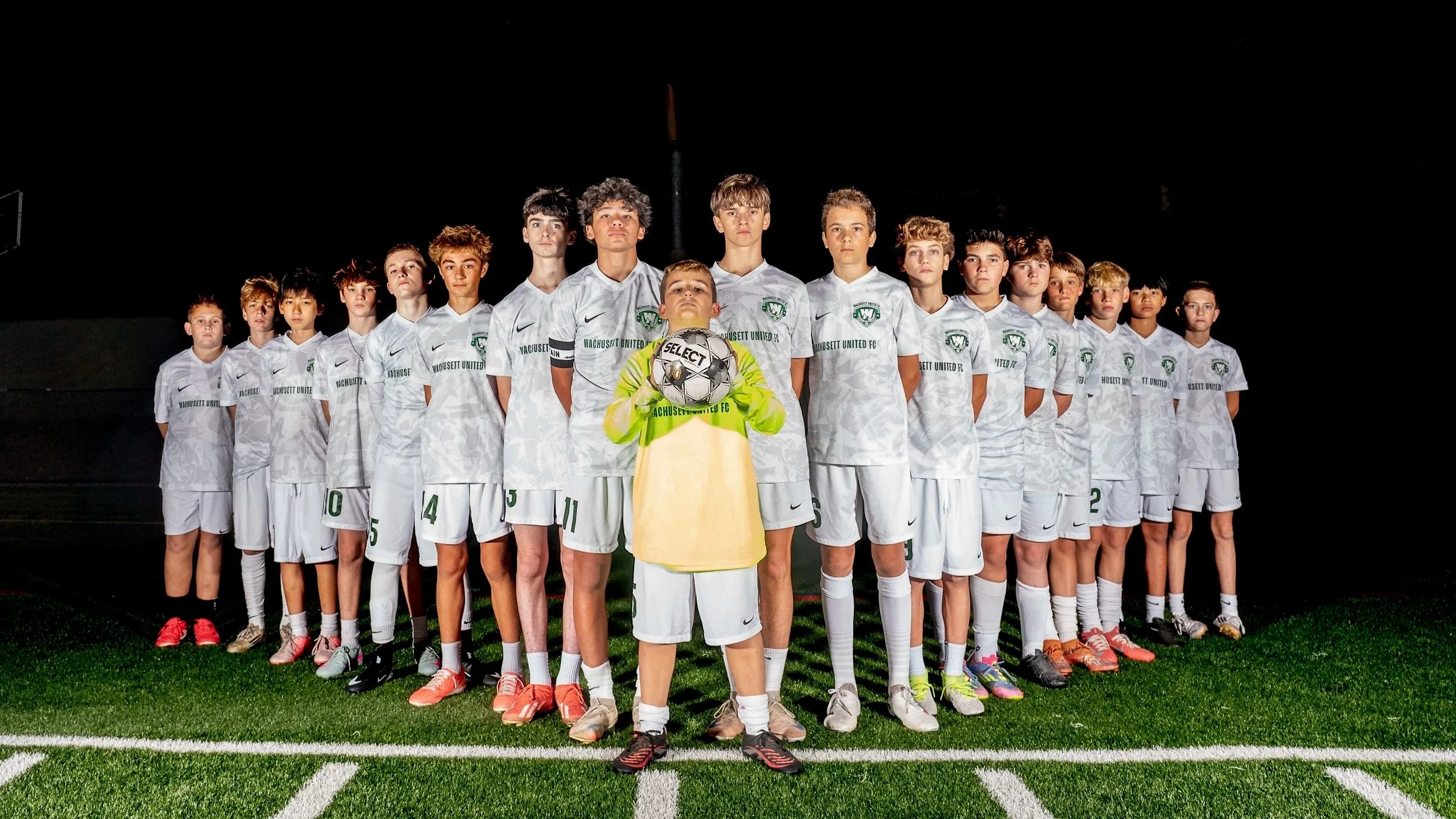 Wachusett United FC boys soccer team posed under stadium lights at night on a turf field in Massachusetts