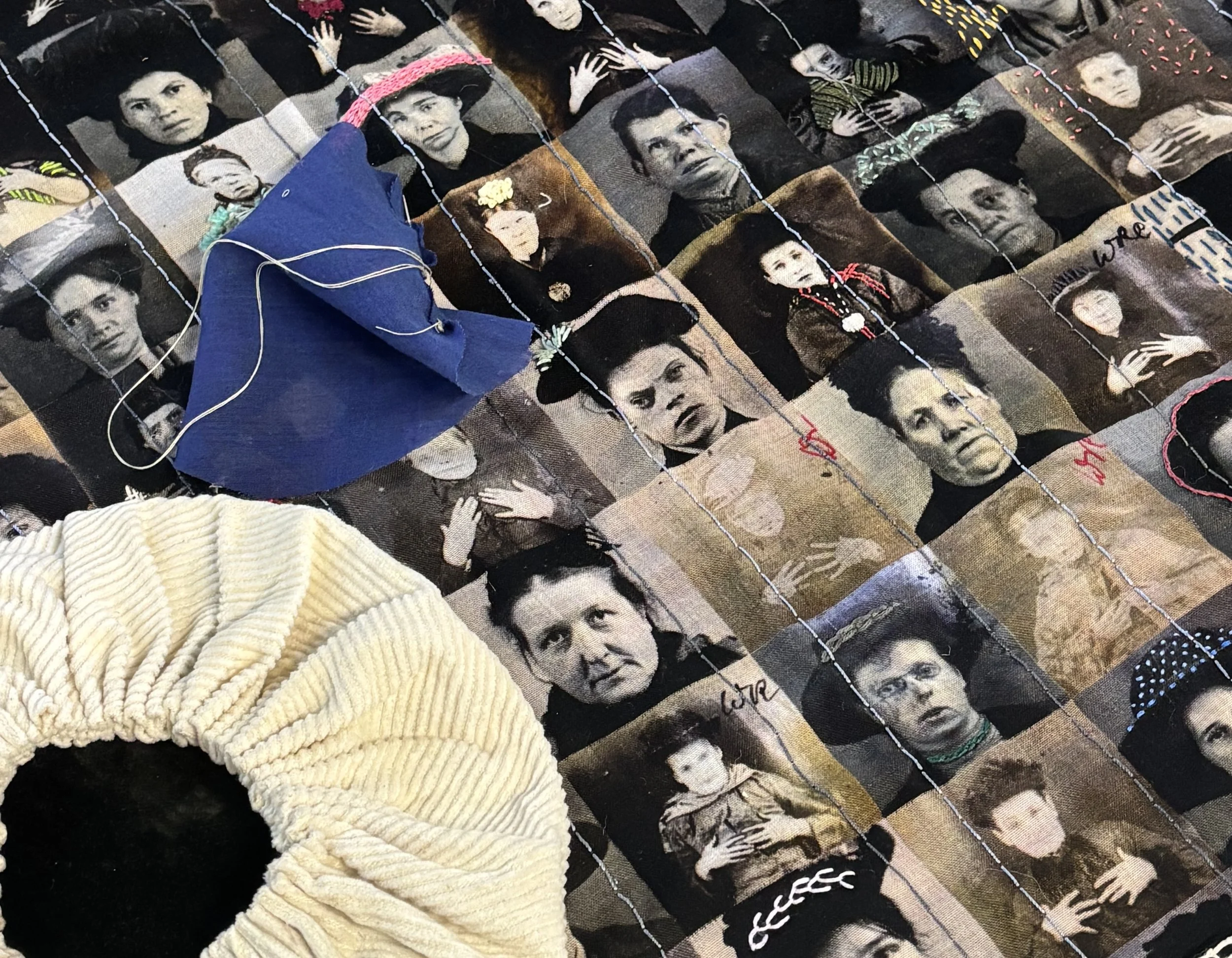 A quilt featuring black-and-white portraits of somber-faced individuals, overlaid with color stitching. A beige, textured circle lies on the left, intersecting a blue fabric piece with a loose white thread.