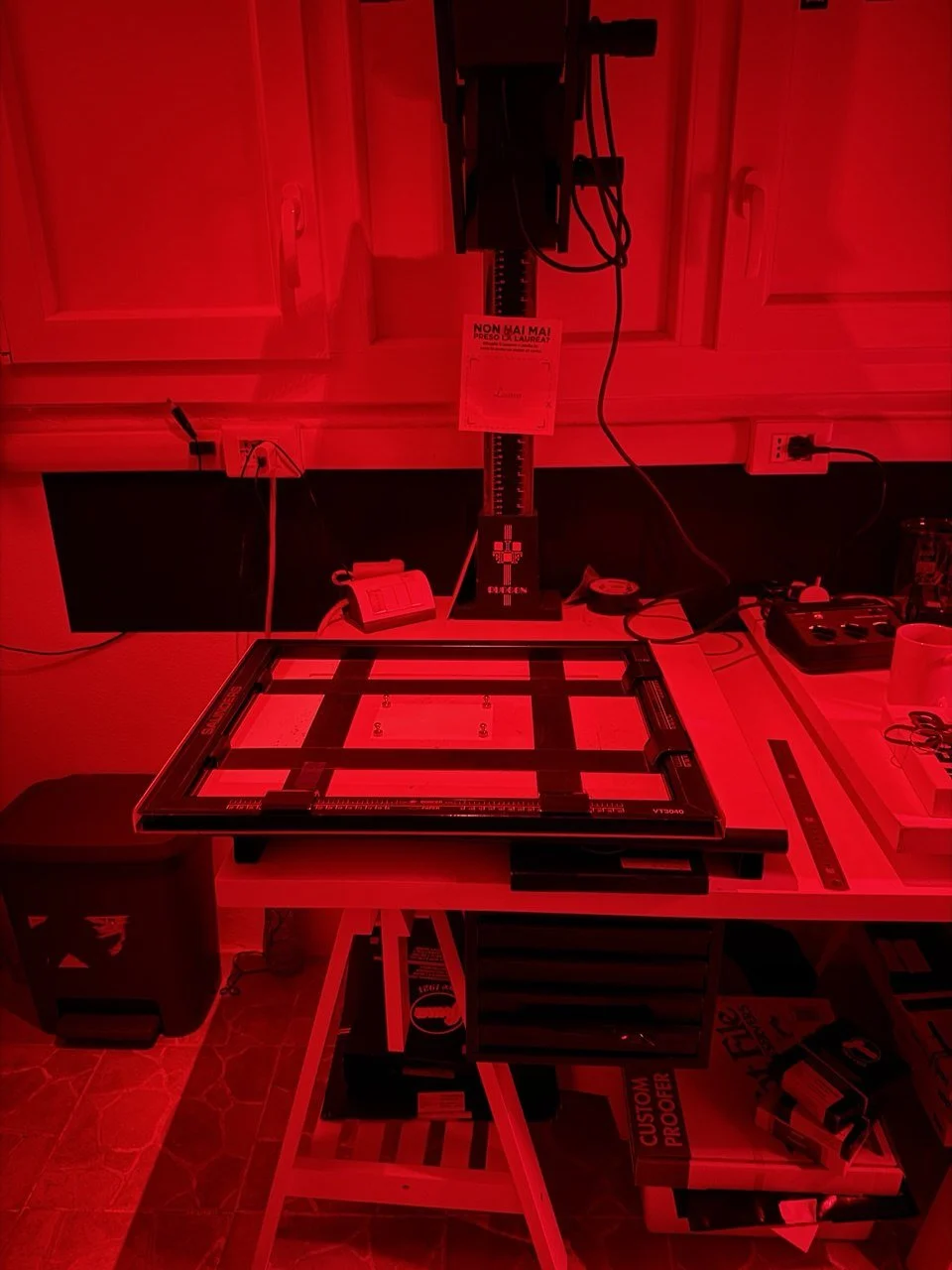 Ingranditore fotografico con luci rosse e materialiper la stampa analogica inn camera oscura.