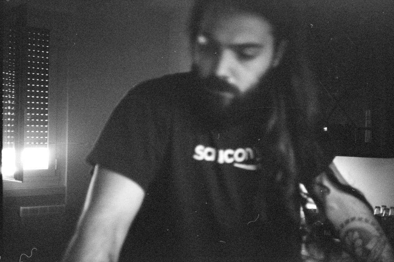 Immagine in bianco e nero di una persona con barba, che guarda verso il basso, con una finestra aperta sullo sfondo