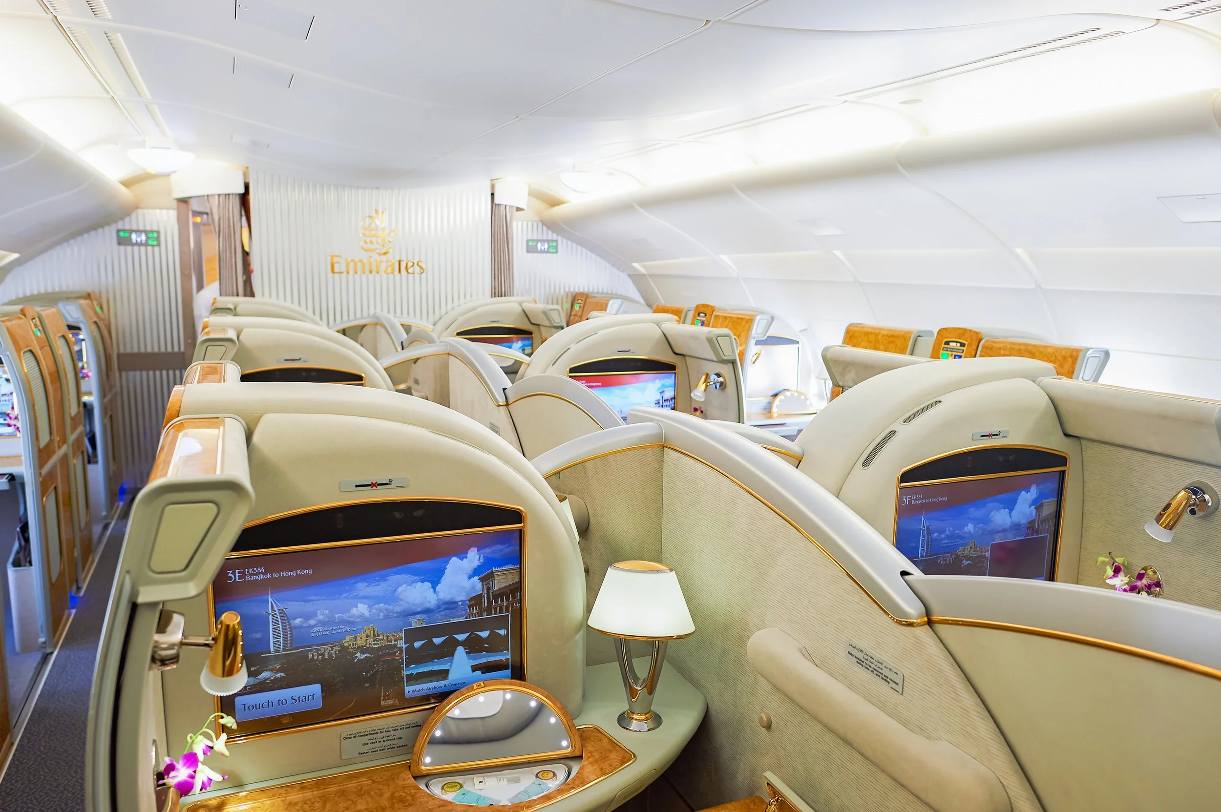 First class or business class cabin on an Emirates airline airplane with spacious seats, personal screens, and elegant decor.