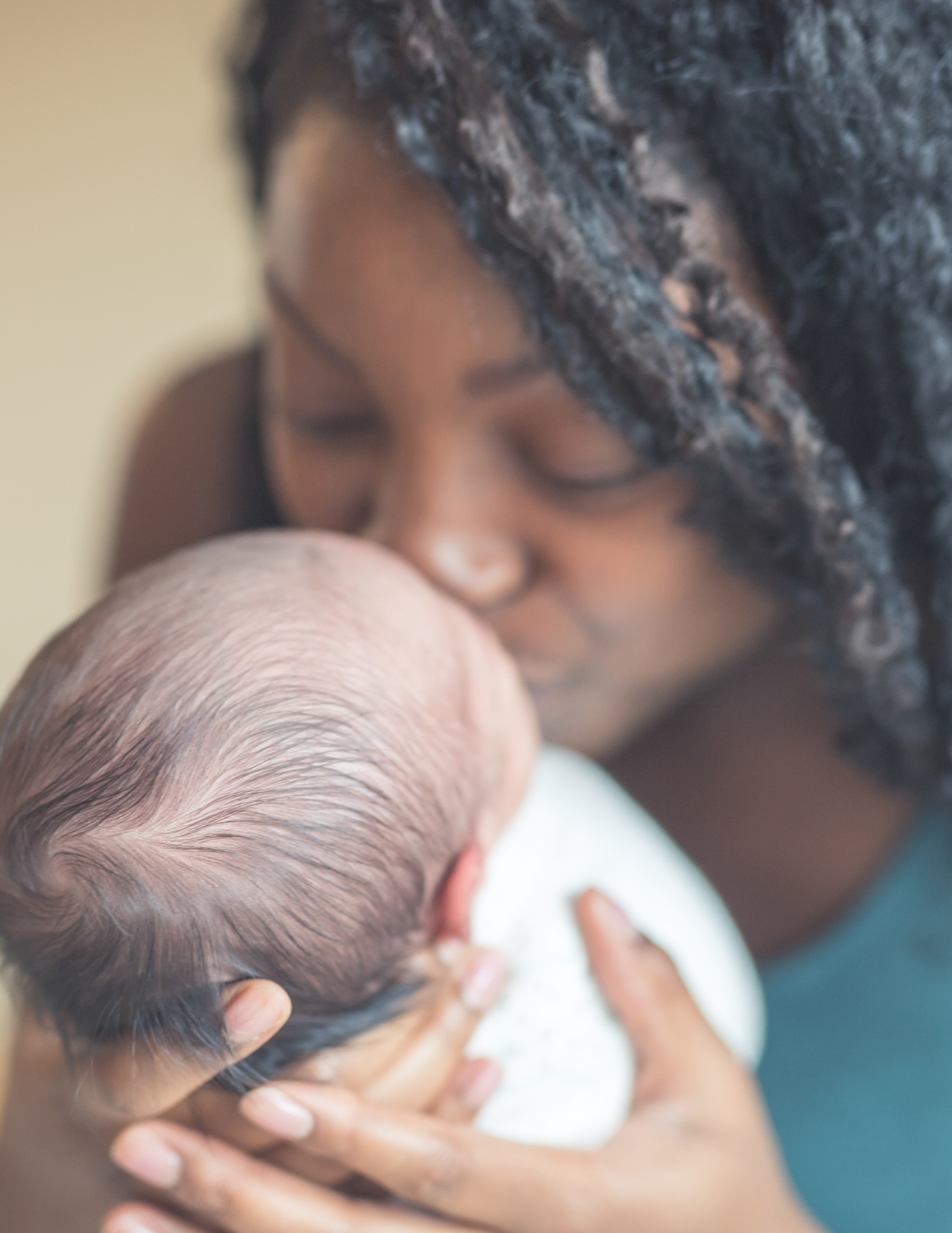 A woman holding a newborn baby close, with the woman kissing the baby's forehead.