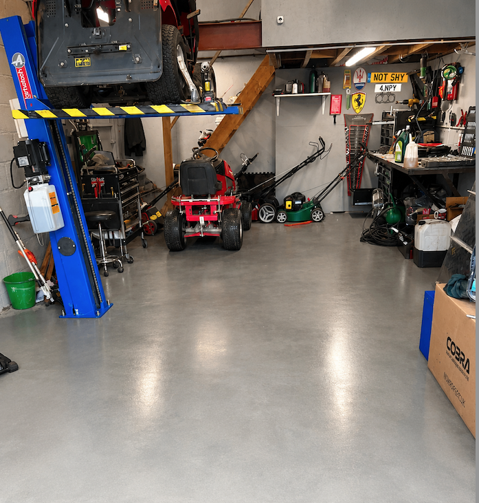 A well-organized garage with a car lift, tools, a lawnmower, and various equipment stored along the walls.