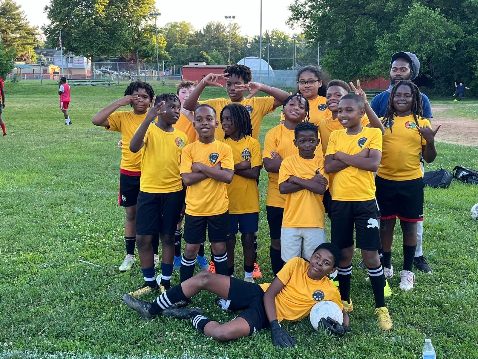 Group of young soccer players wearing yellow jerseys posing on a grassy field.