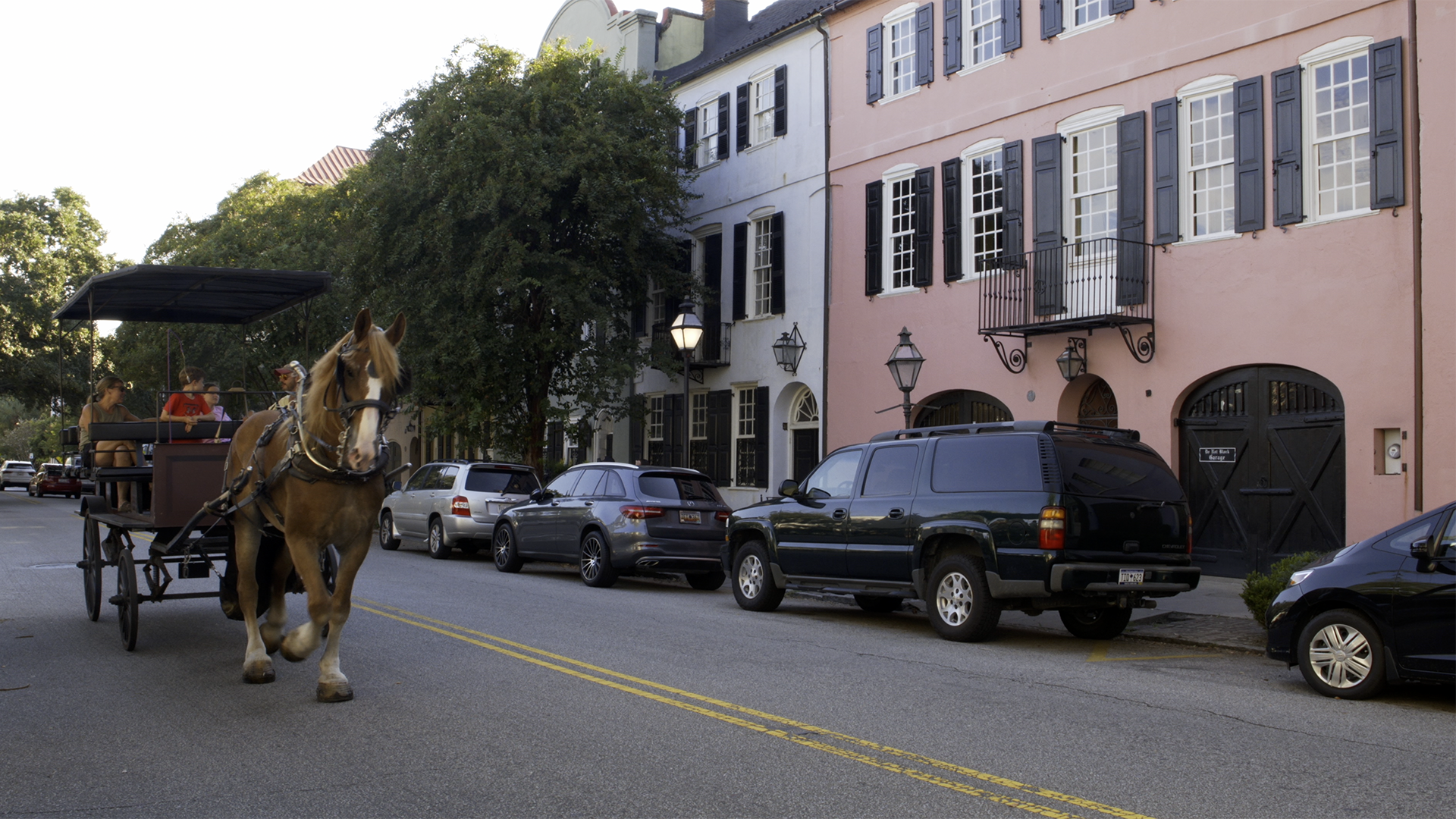 Street scene with horse-drawn carriage, historic buildings, and parked cars.