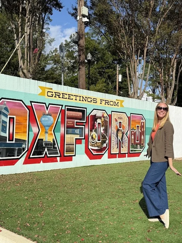 Darley Newman poses in front of a welcome mural to Oxford, Mississippi, located in the alley off North Lamar Boulevard behind the Square, near The End of All Music.