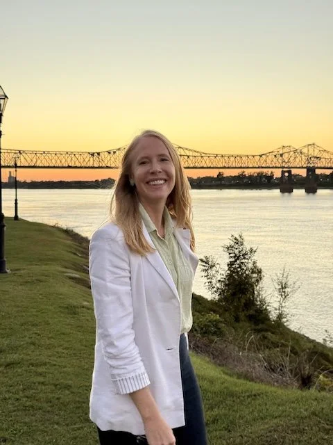 Darley Newman at golden hour along the Mississippi River in Natchez, with the bridge stretching across the horizon above Under-the-Hill.