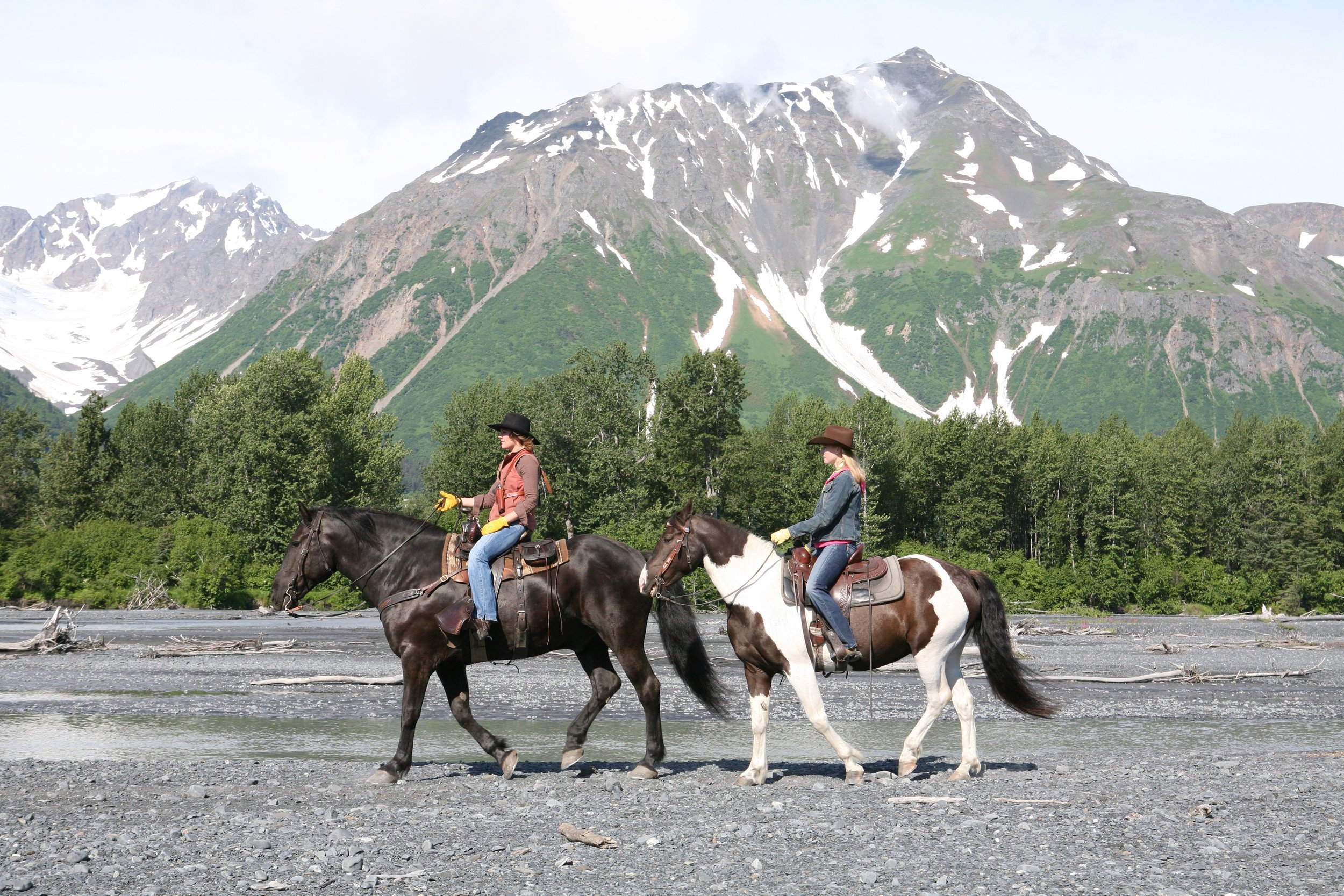 Darley Newman Travels with Darley Equitrekking Vacations: Two people horseback riding in front of snow-capped mountains and forest