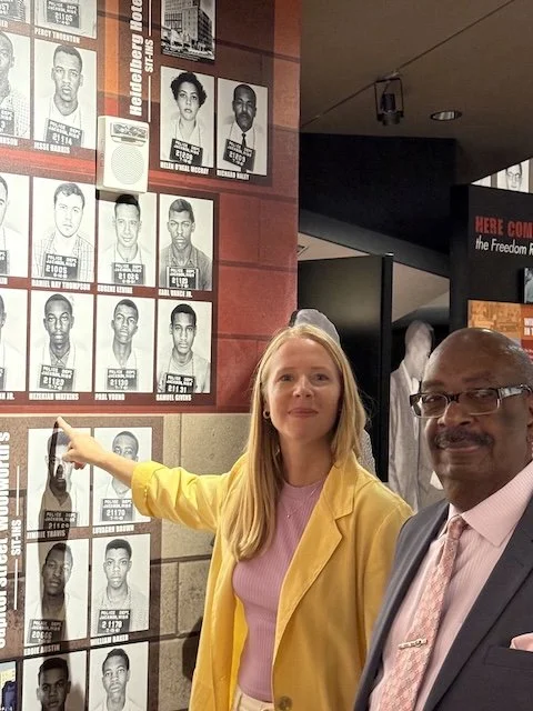 Darley Newman stands with civil rights activist Hezekiah Watkins inside the Mississippi Civil Rights Museum, pointing to his mugshot on the museum’s wall—an arrest photo taken when he was jailed as a teenager for participating in the Freedom Rides.