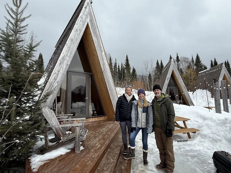 Darley Newman with owners Geneviève Côté and Jonathan Casaubon at Farouche Nordic Farm, discovering their cozy A-frame glamping chalets set in the snowy Laurentians.