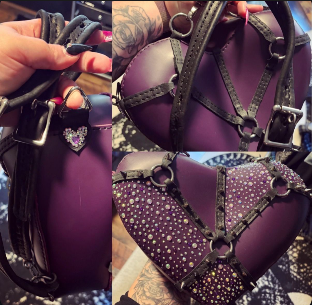 A purple leather heart bag with black leather harness covered in spikes and rhinestones