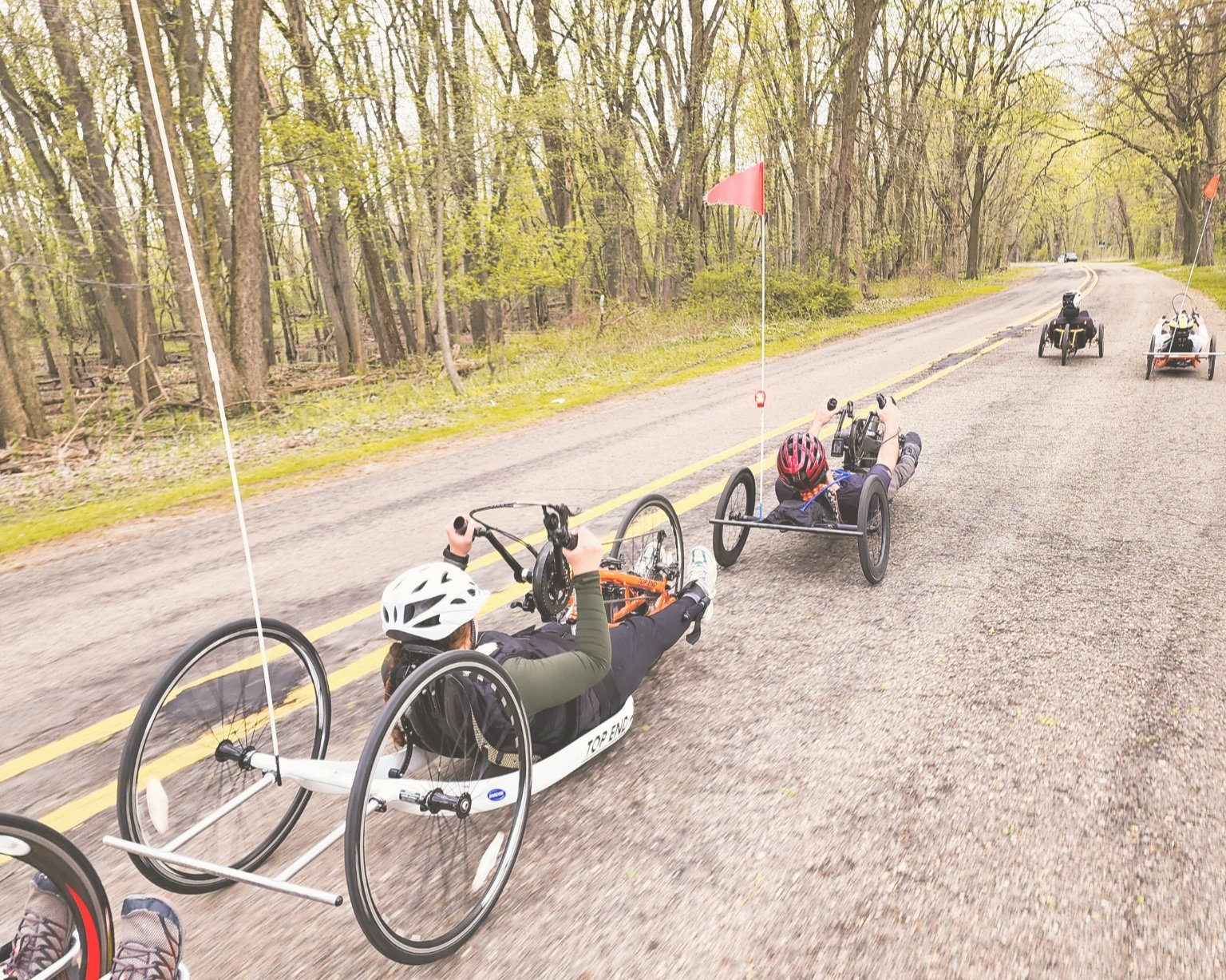 Group of people riding recumbent tricycles on a rural road surrounded by trees