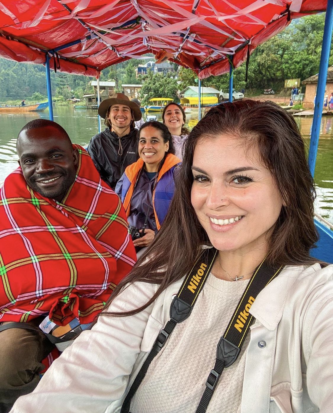 Group of five people smiling on a boat ride with a canopy over water and green landscape in the background.