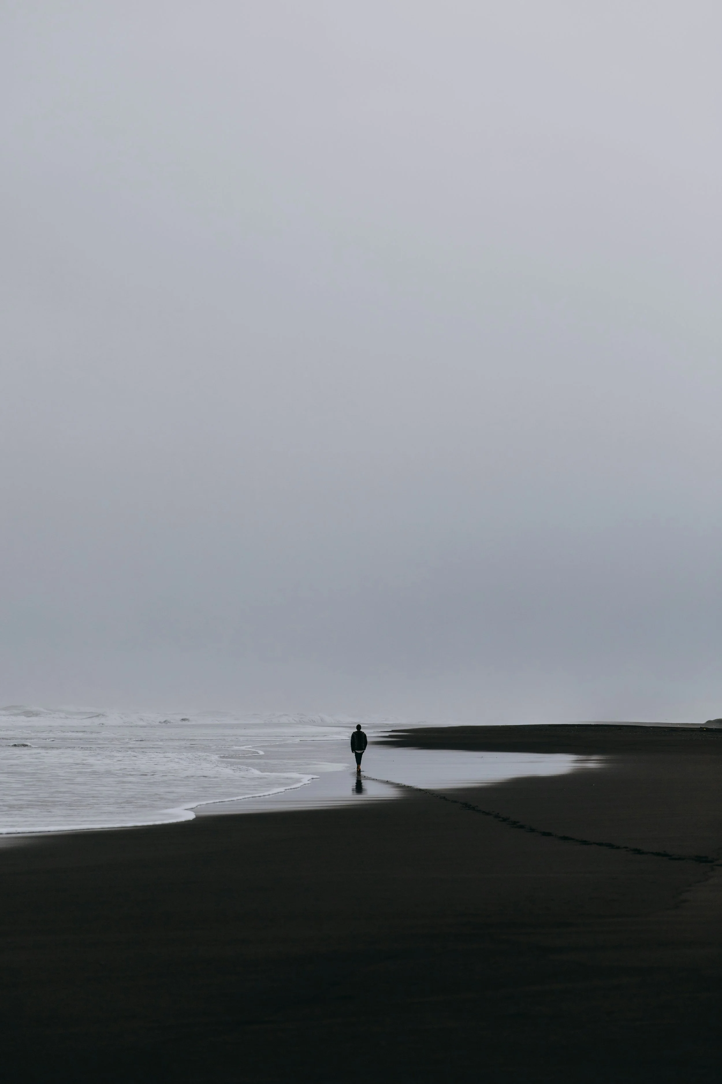 Solitary figure walking along a quiet shoreline at dusk, reflecting themes of early attachment patterns, chronic illness, emotional self-reliance, and the experience of learning to receive care.