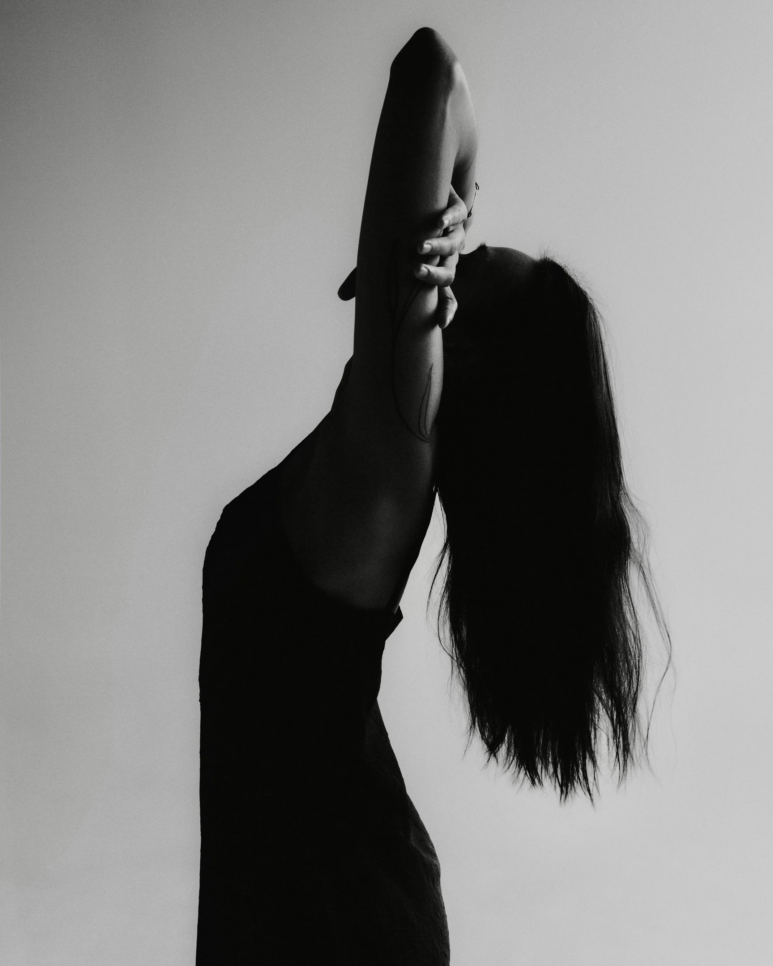 Black-and-white image of a person gently stretching with one arm raised, reflecting how safety in the body can feel gradual and embodied.