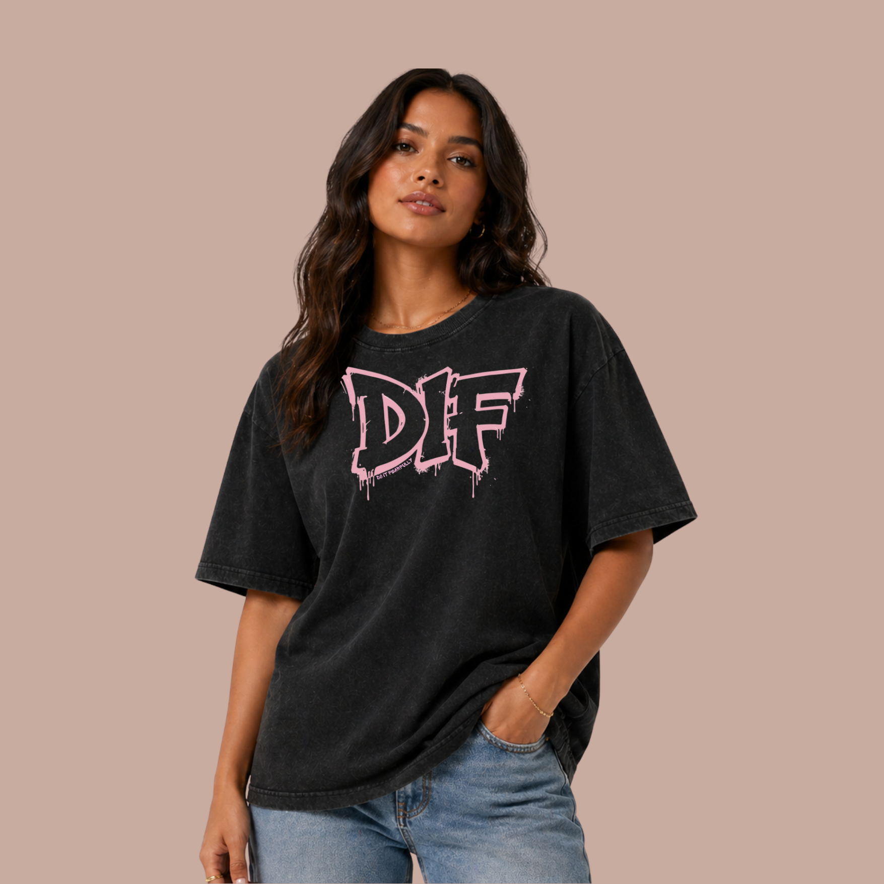 A young woman with wavy dark hair wearing a black oversized T-shirt with pink and white graphic text and light blue jeans, standing against a beige background.