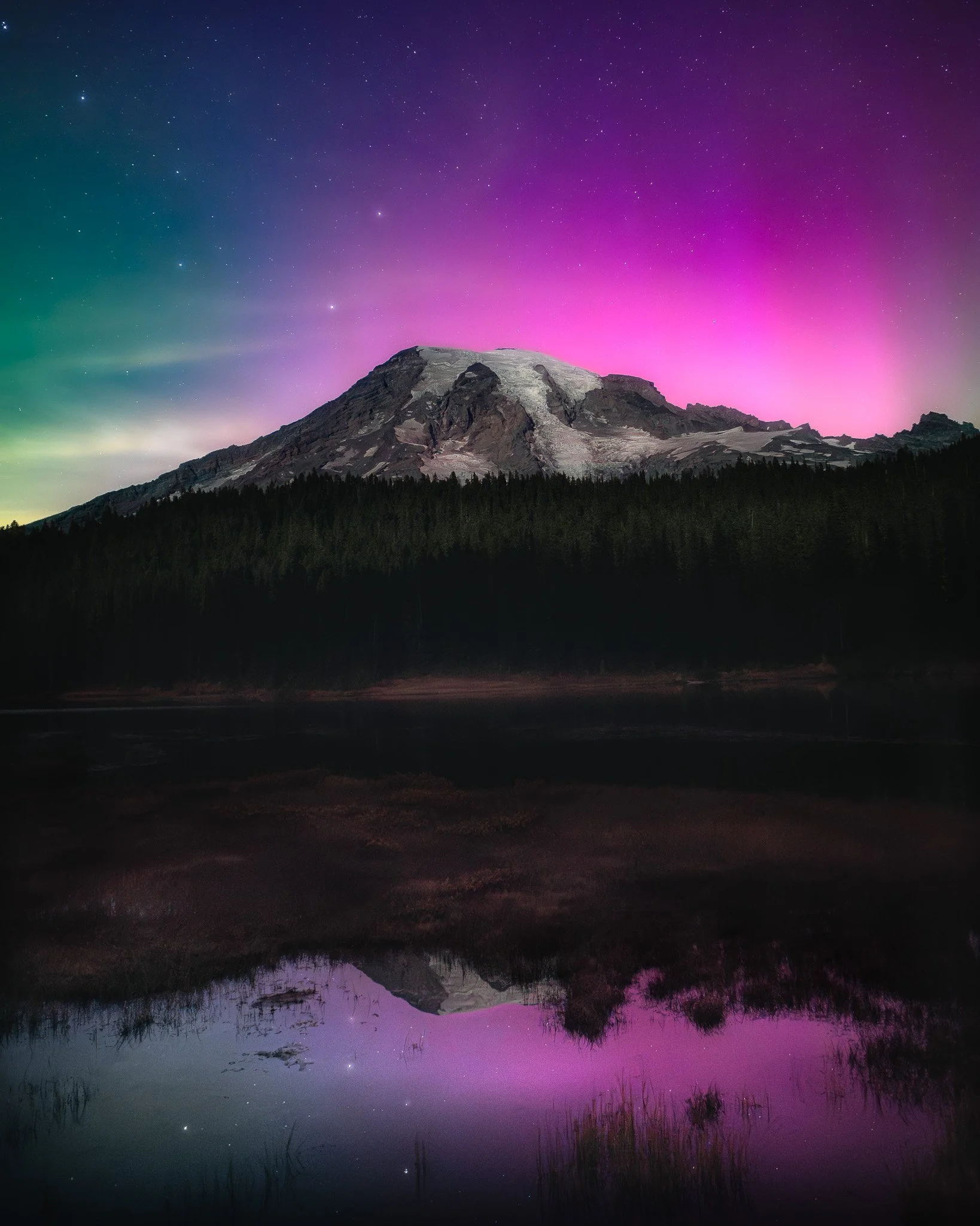 Mountains with colorful aurora borealis and stars in the night sky, reflected in a lake