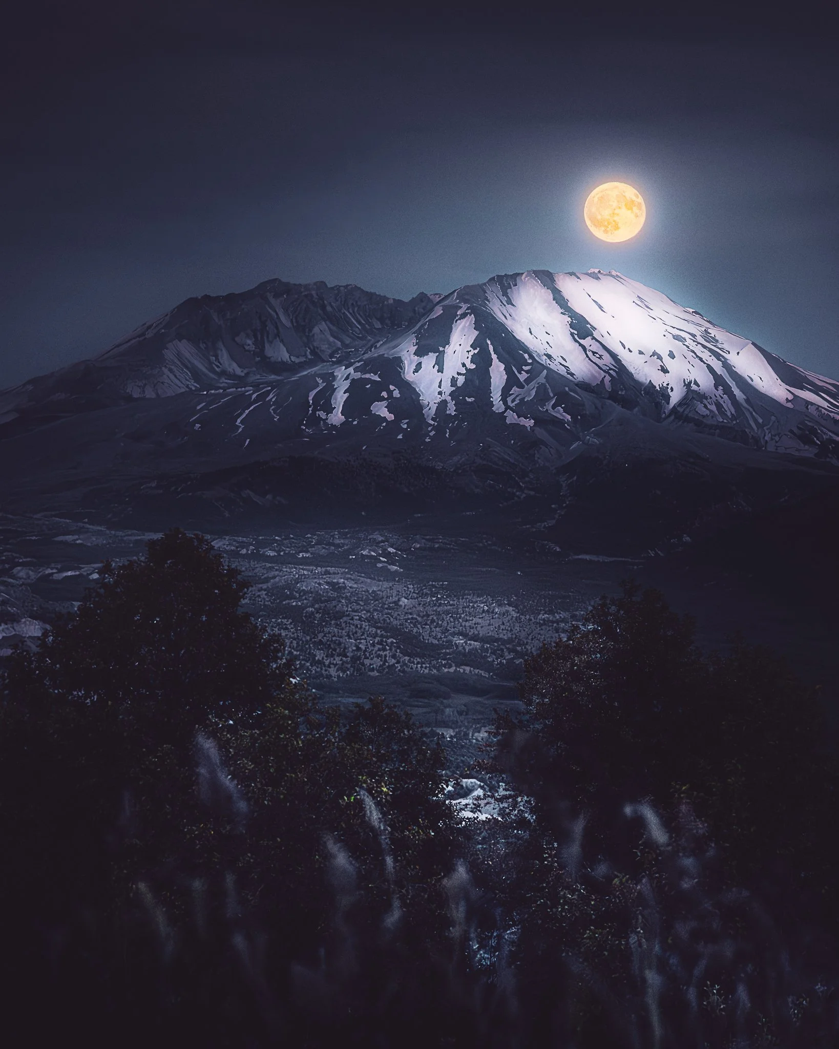 A snow-capped mountain under a full moon at night, with dark trees and landscape in the foreground.