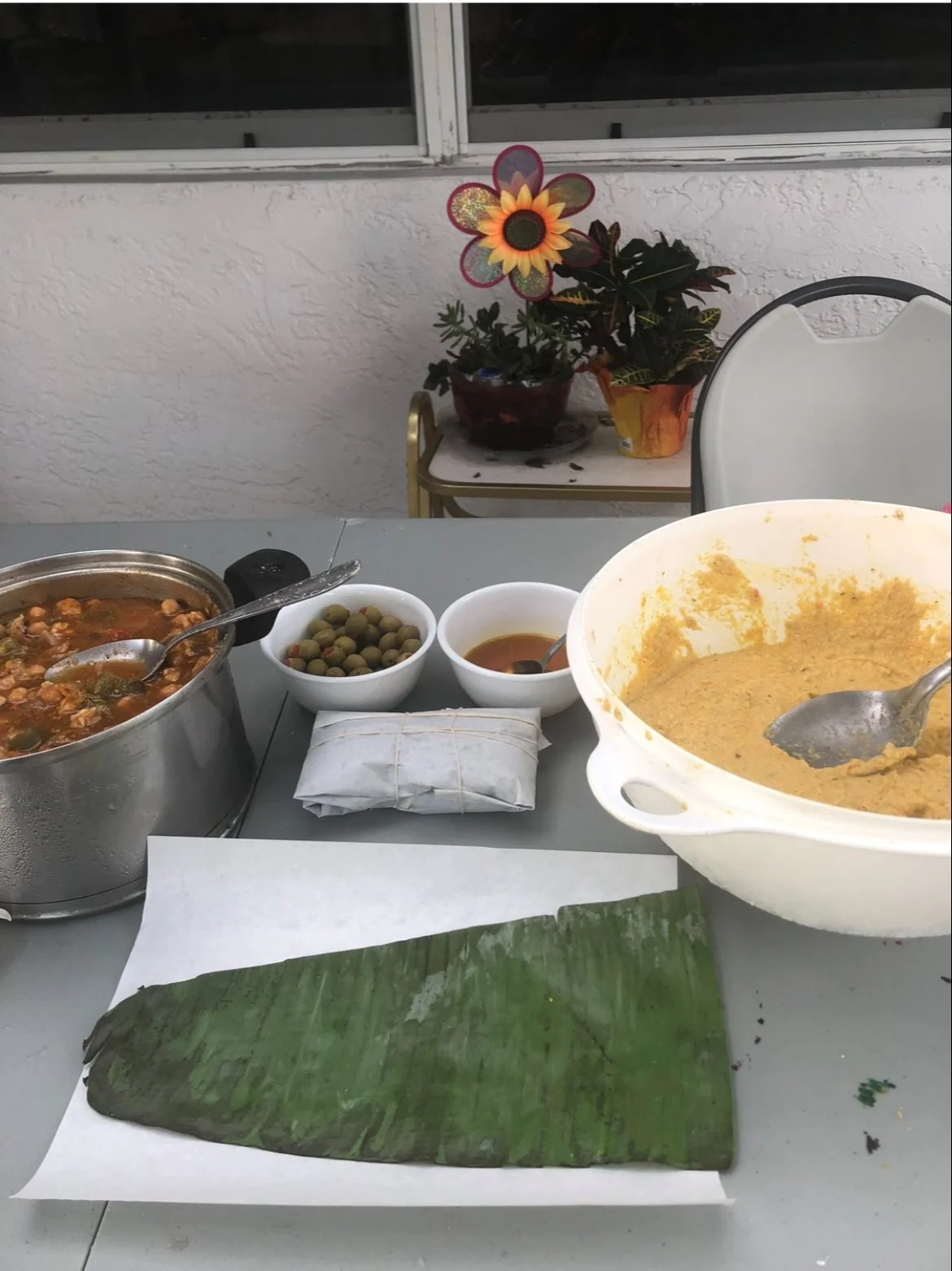 Preparación de pasteles. En una mesa hay el relleno, las aceitunas, la masa, y la hoja de plátano.