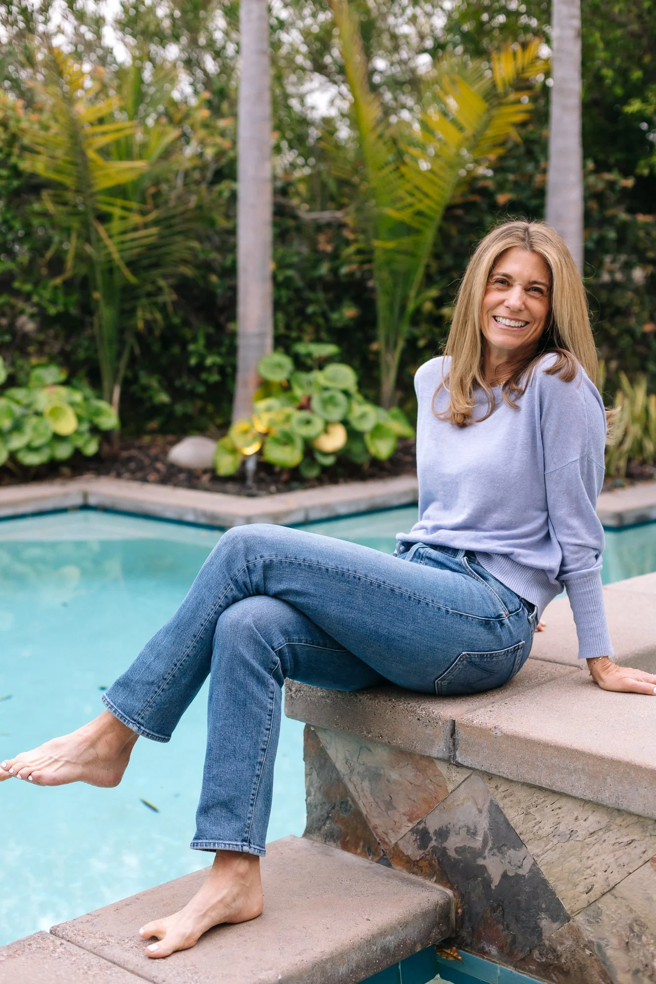 Ilene Schaffer seated poolside in a tropical garden, smiling in a moment of calm and connection — reflecting her coaching approach to clarity, wellbeing, and intentional living.