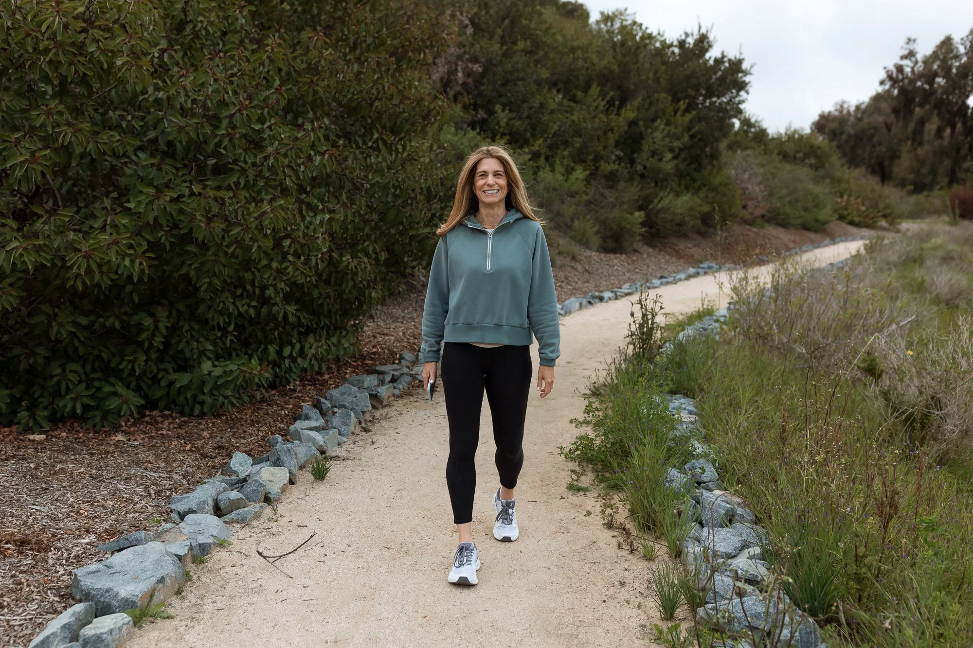 Ilene Schaffer walking a winding trail surrounded by greenery — embodying her coaching approach to movement, reflection, and nature-connected wellbeing.