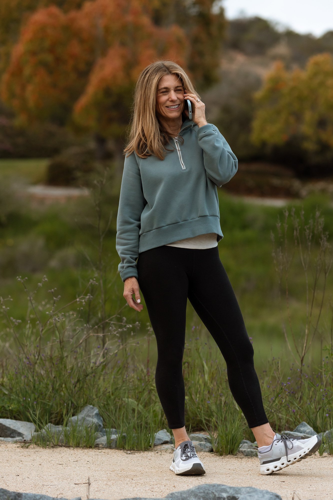 Ilene Schaffer walking and talking on a fall trail, smiling during a phone conversation — embodying her coaching style of connection, clarity, and real-life presence.