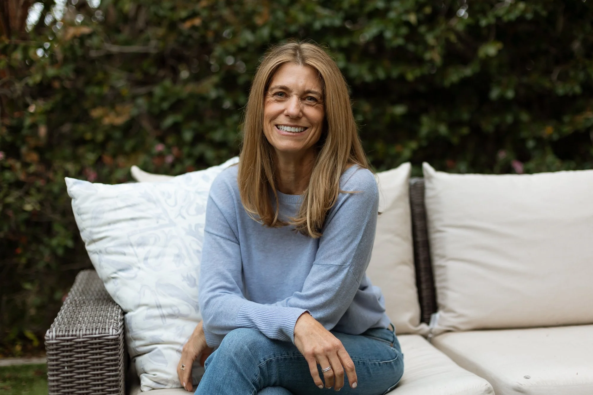Person seated outdoors on a cushioned bench, smiling in a nature-filled setting — representing Ilene Schaffer’s coaching focus on warmth, presence, and connection in relaxed environments.