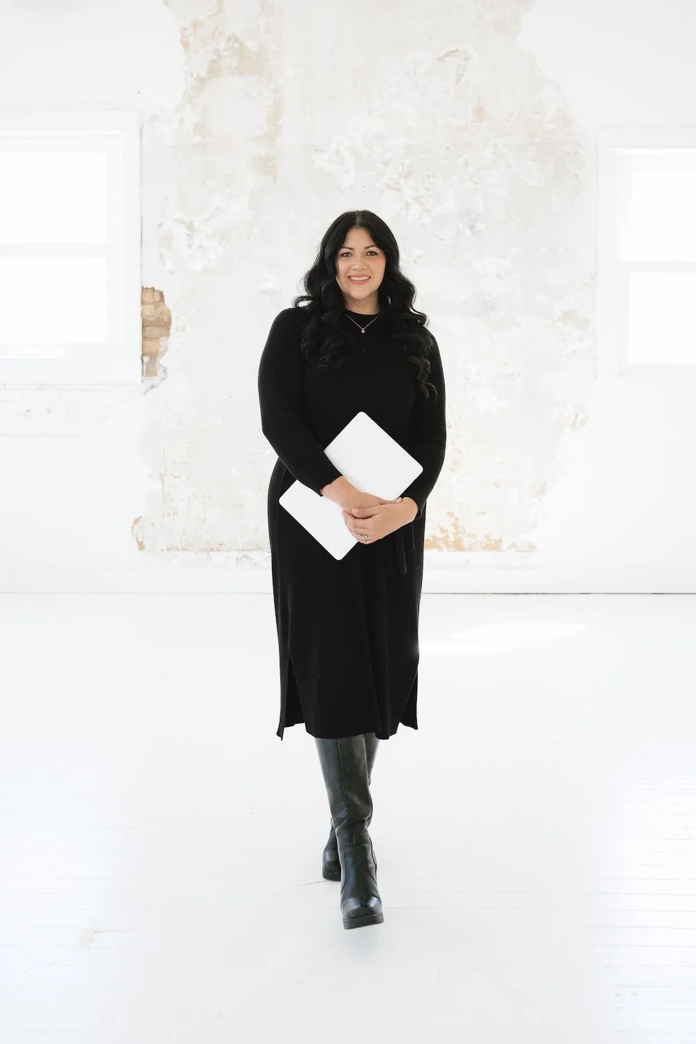 Gabrielle standing and smiling while holding a closed laptop.