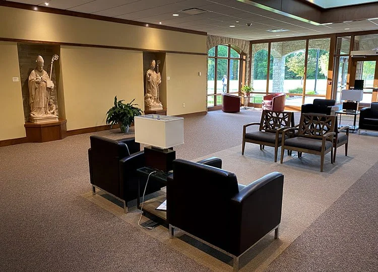Lobby area with armchairs, wooden chairs, and statues of religious figures on wall niches.