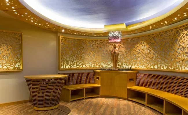 Circular seating area with wooden benches and decorative golden wall panels, illuminated by soft lighting and a central statue with a lampshade