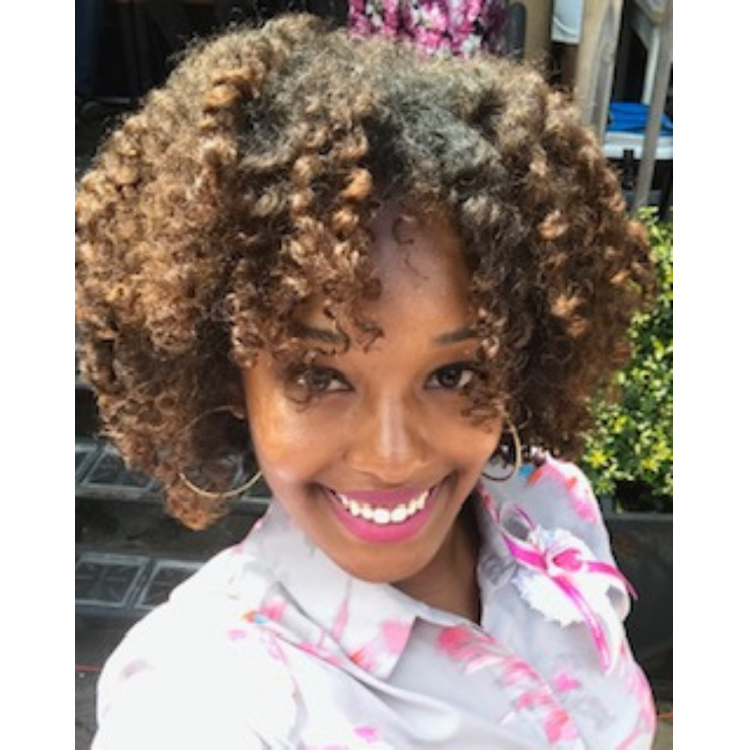 Smiling woman with curly, brown-toned hair, wearing large hoop earrings and a floral-patterned top.