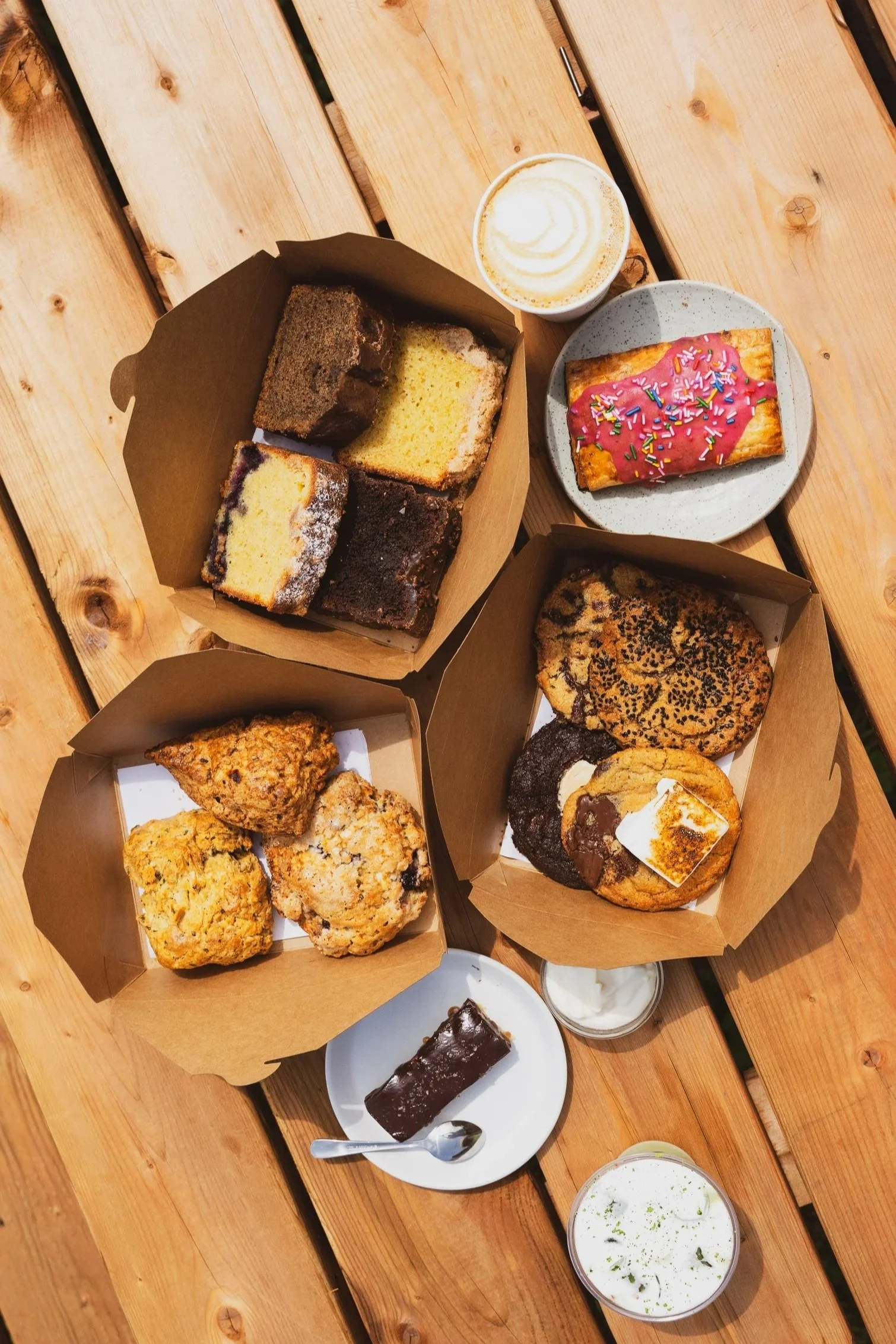Des gâteaux variés, un café latte, un chocolat chaud, et des milkshakes sur une table en bois.