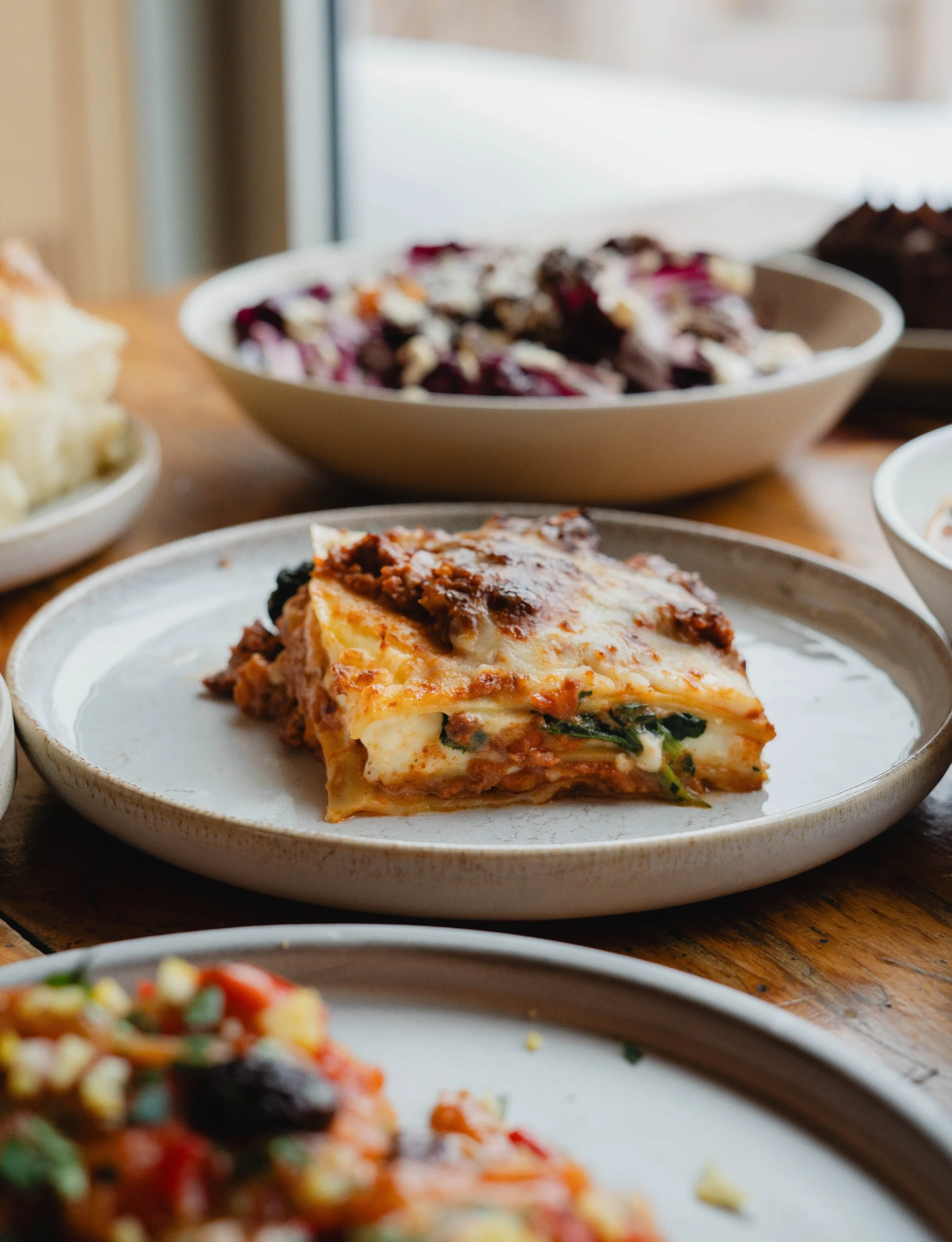 Une assiette de lasagne avec une couche de fromage gratiné, entourée d'autres plats de cuisine sur une table en bois.