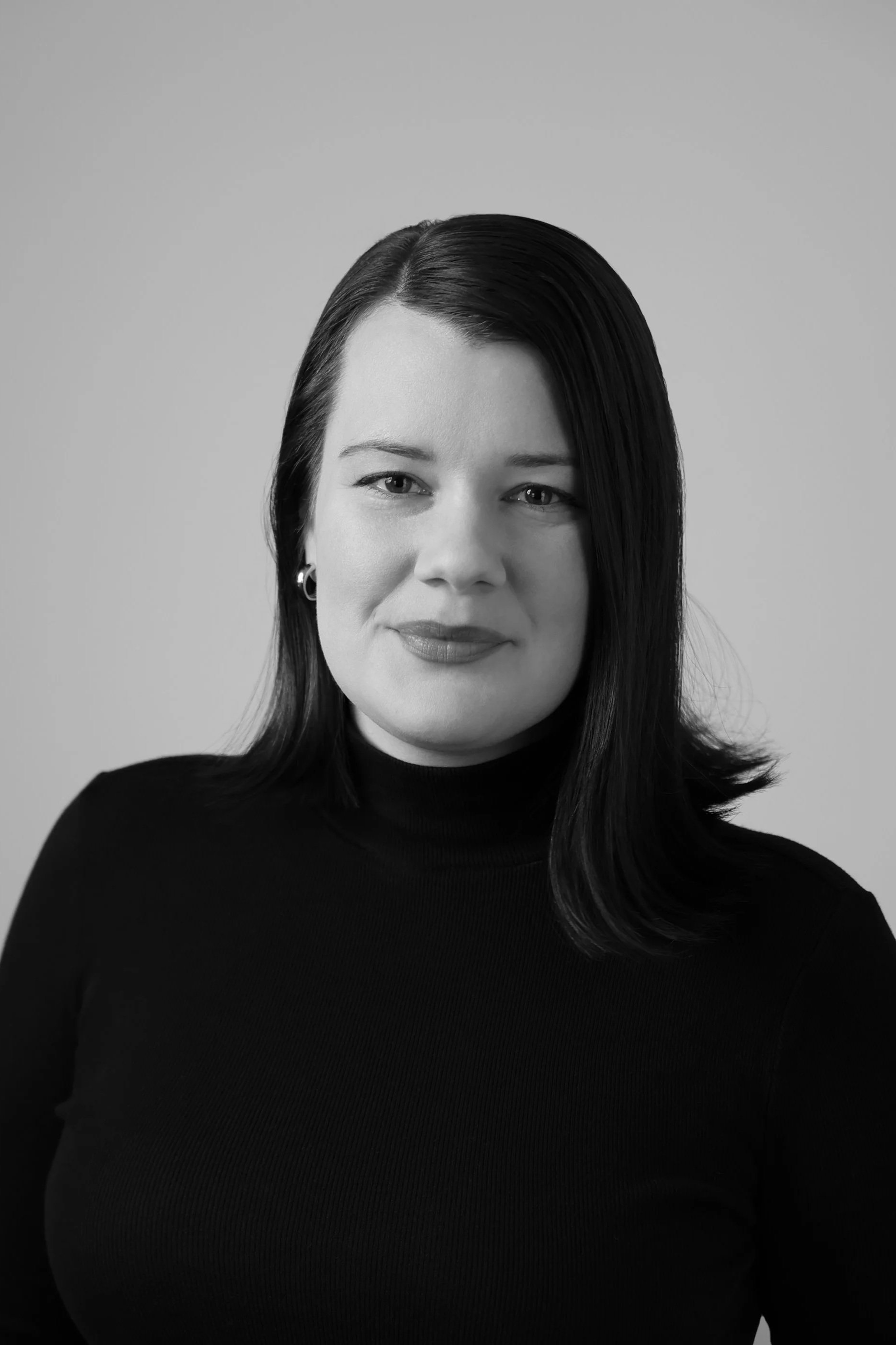 Black and white portrait of a woman with long dark hair, wearing a black turtleneck, looking directly at the camera with a slight smile.