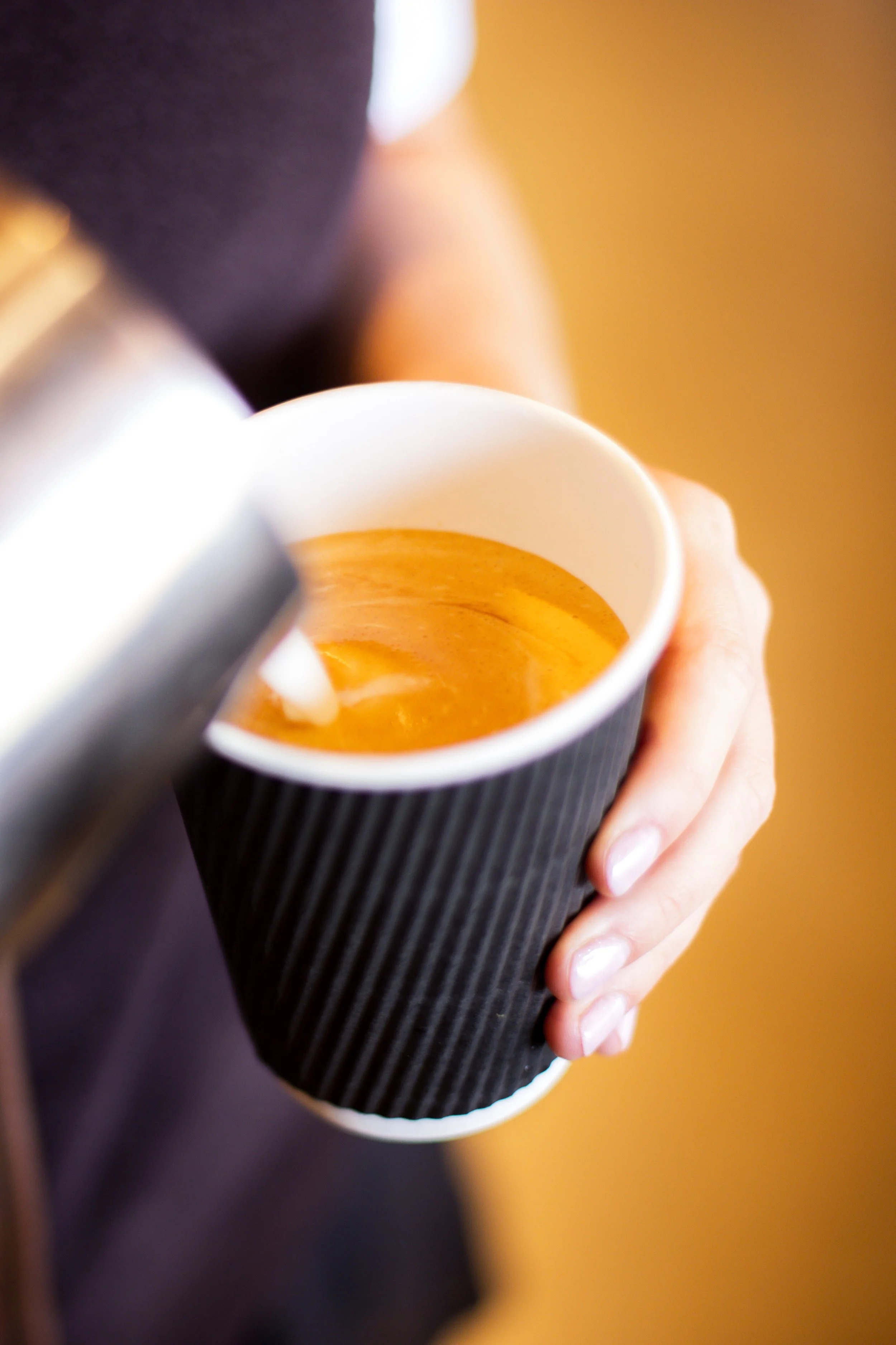 Close-up of a person's hand holding a paper cup with a frothy coffee drink inside.